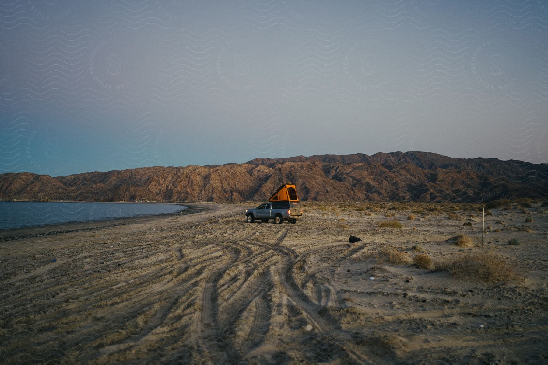 A pickup truck with a camper on a lakeside beach.