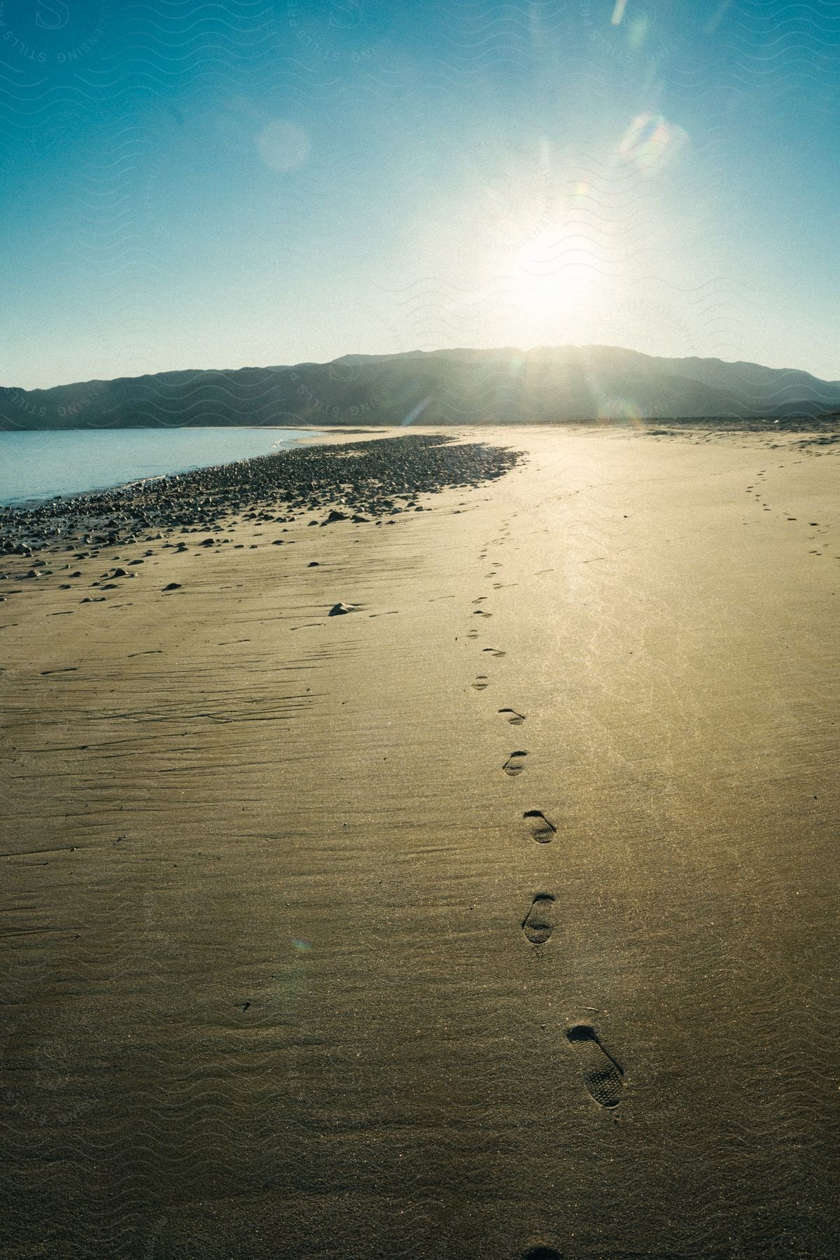 View Of Footprints In Beach Sand With The Morning Sun On The Horizon