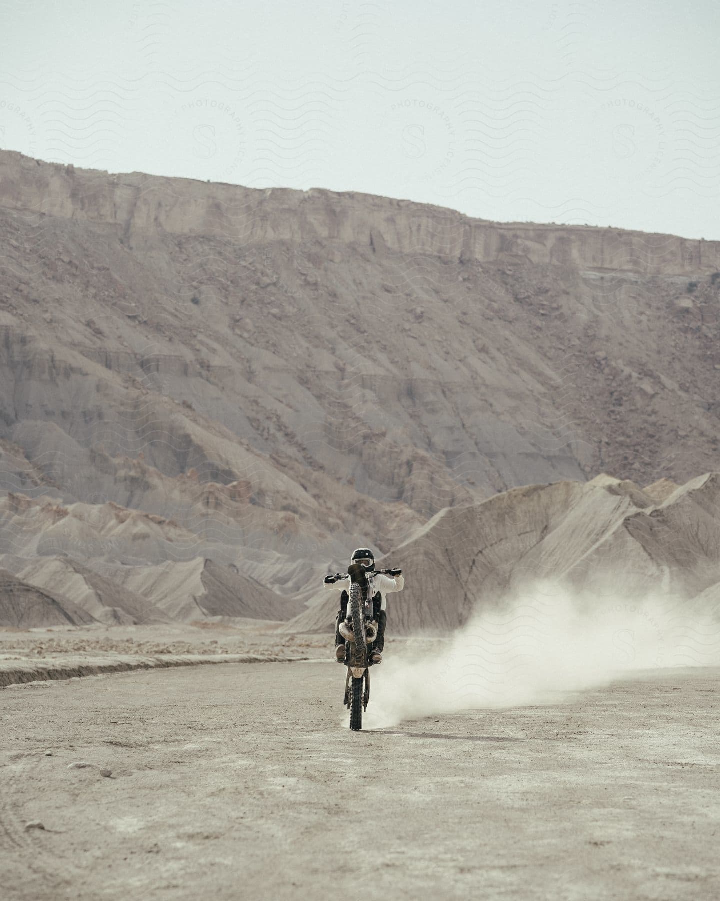 A person wearing goggles rides a motorcycle on the back wheel through the desert.