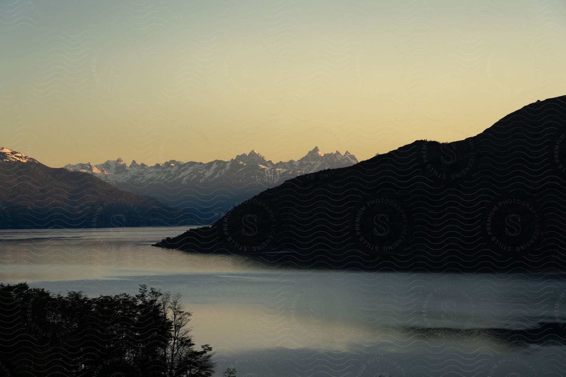 Panorama of peaks and snow-covered mountains along the banks of a river under a dawn sky.