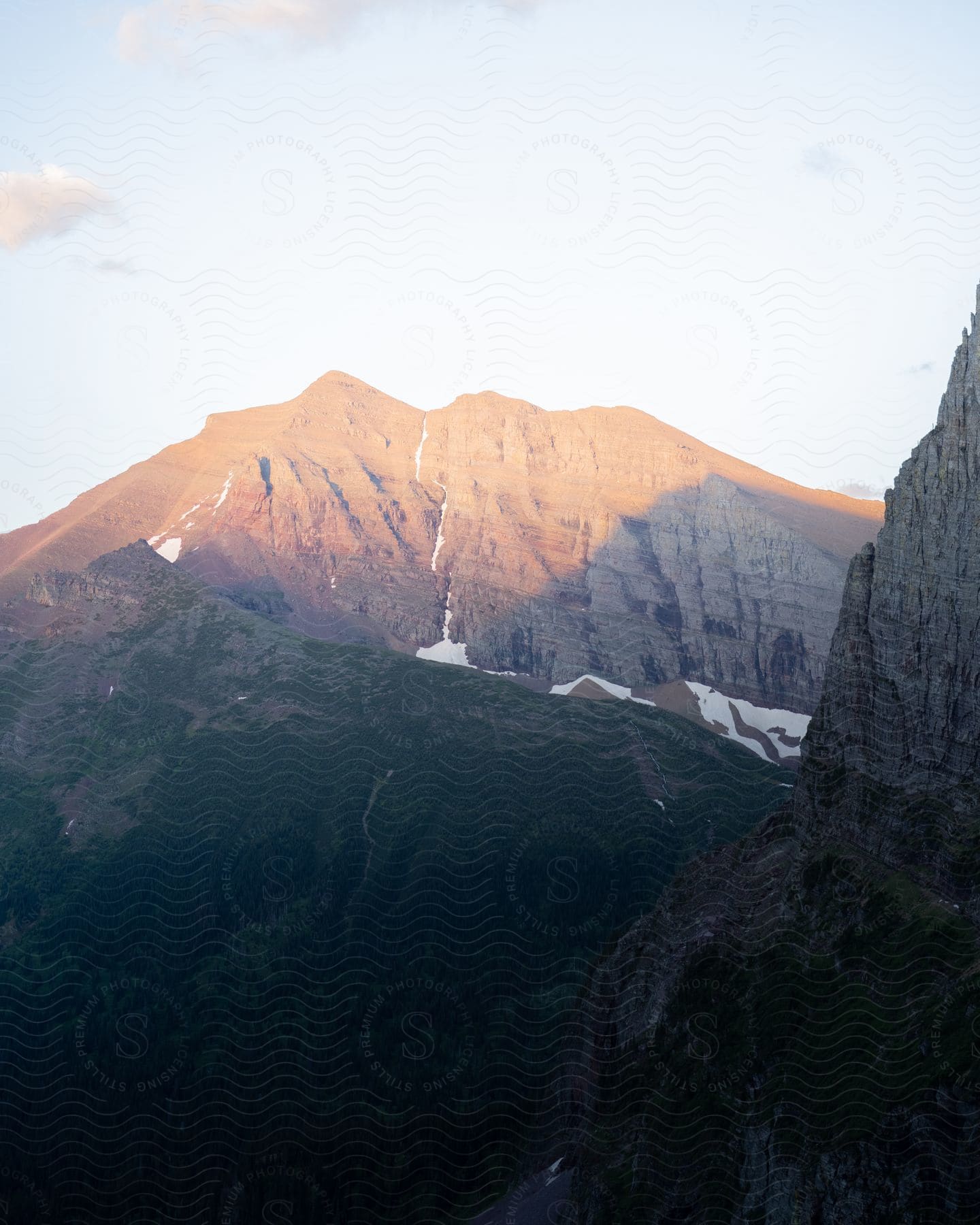 Aerial landscape of mountains and peaks with vegetation and snow under a morning sky.