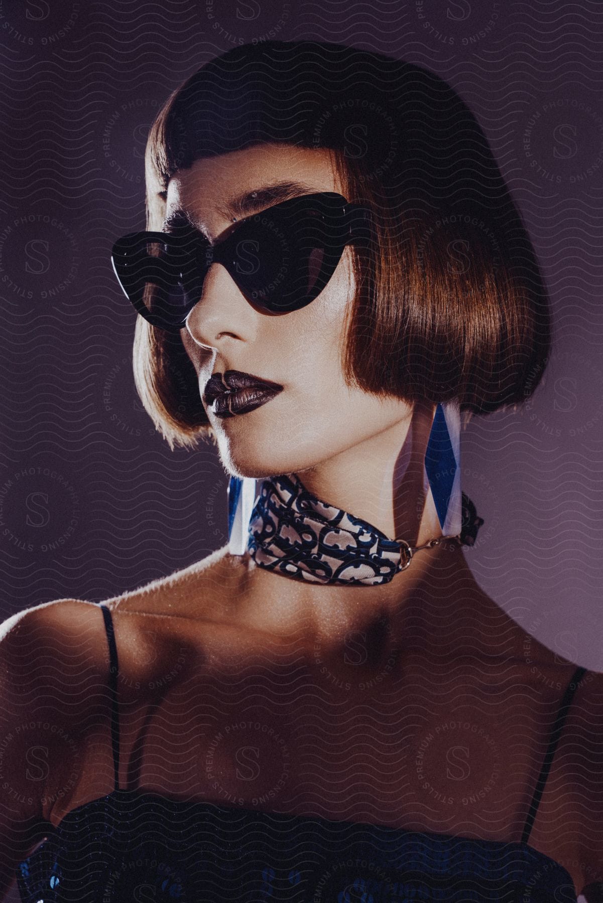 Stock photo of a woman wearing oversized sunglasses, a patterned neck scarf, and dark lipstick, with a sharp bob haircut.