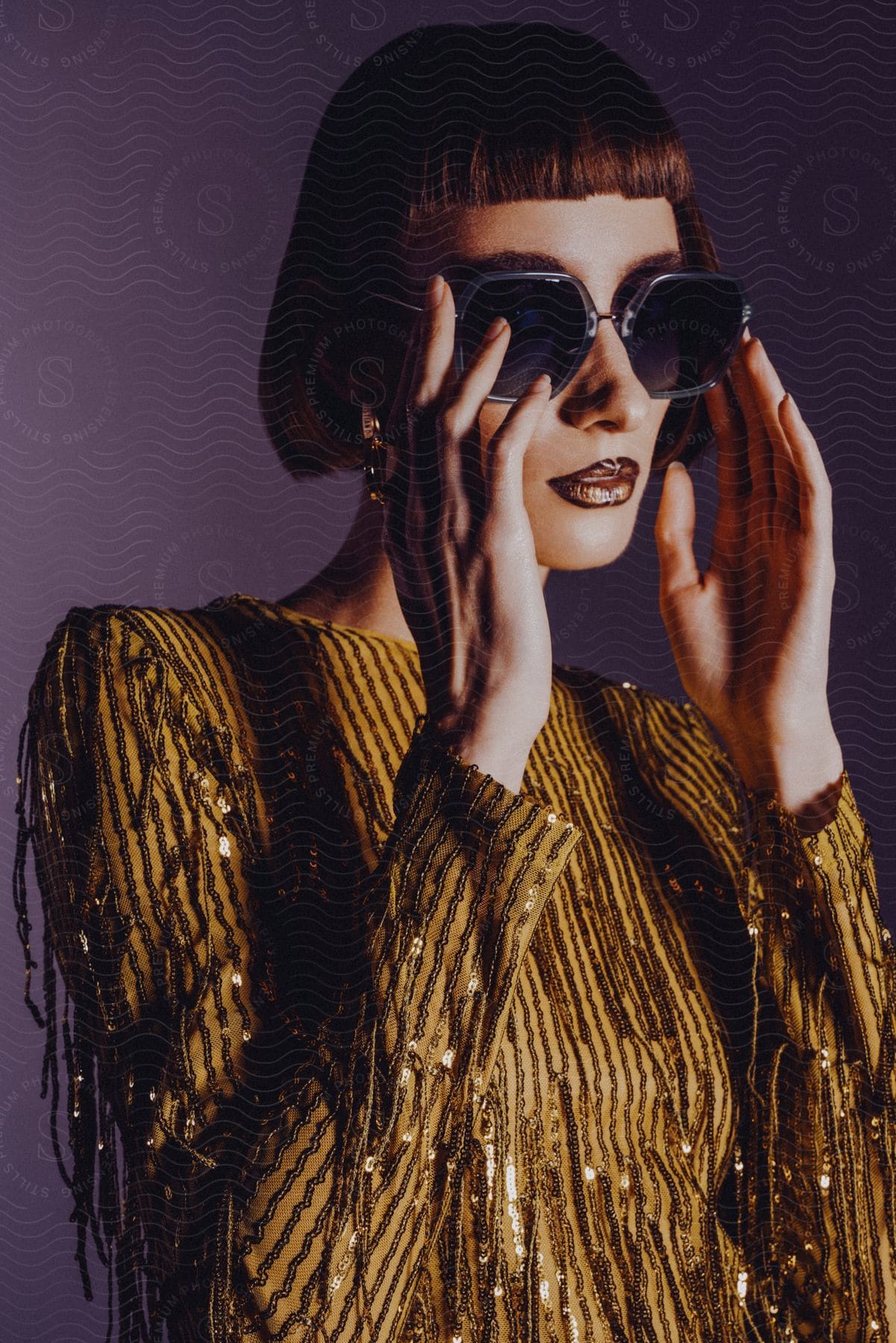 Model woman posing with hands on sunglasses and wearing a golden sequin dress.