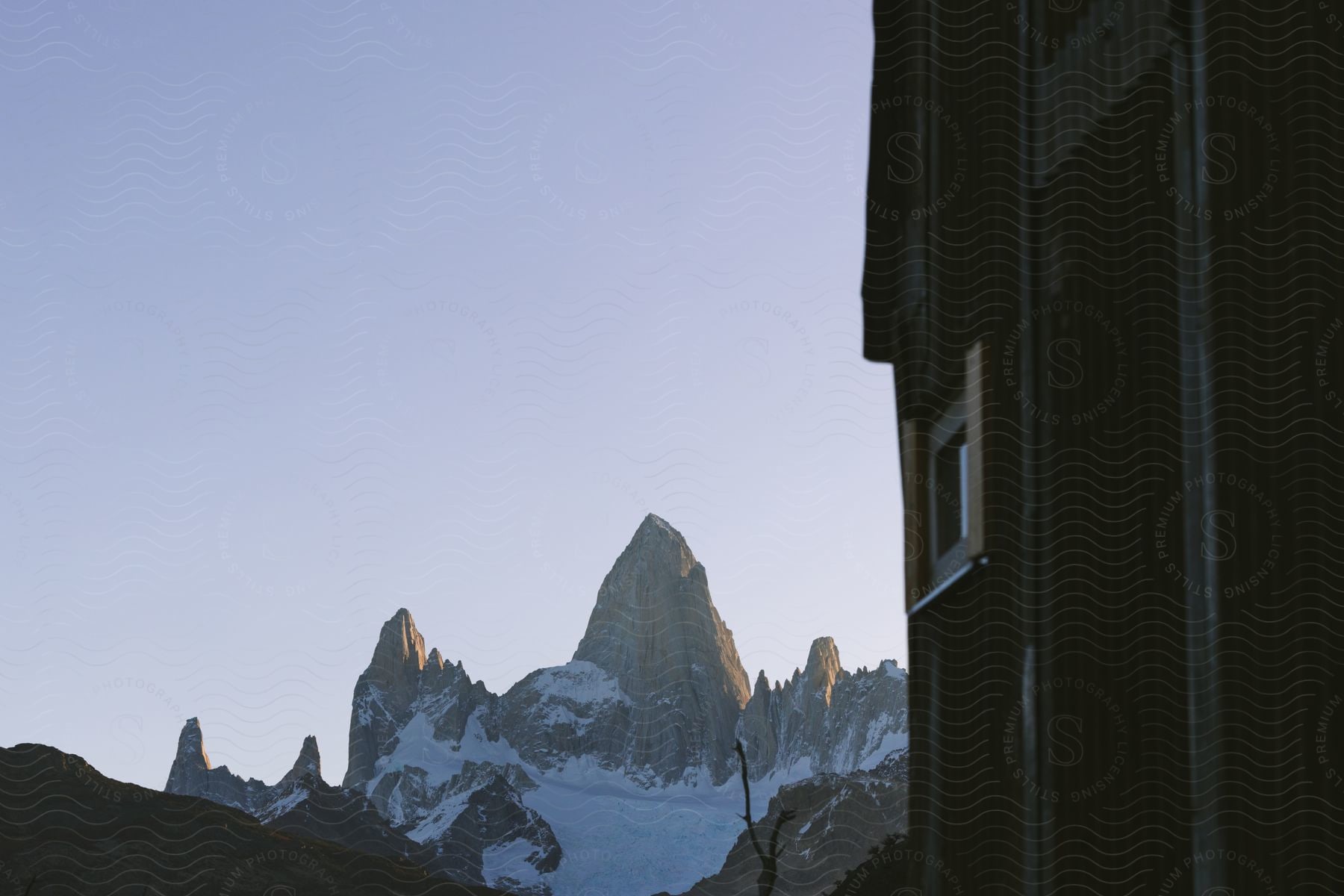 A picturesque mountain cabin nestled in the foreground of a stunning snow-capped mountain range.