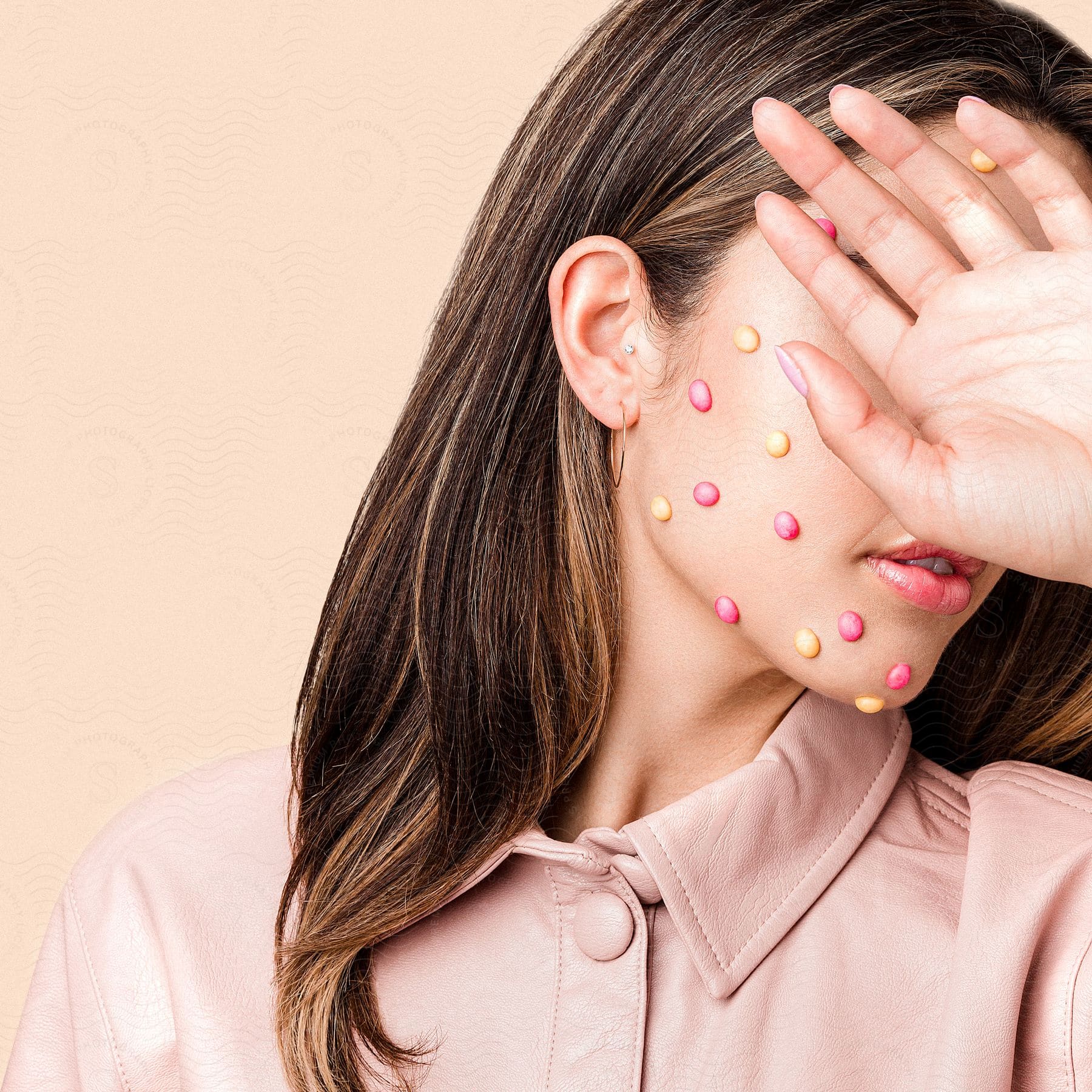 A woman with colored dots on her face puts her hand in front of her eyes as she turns her head