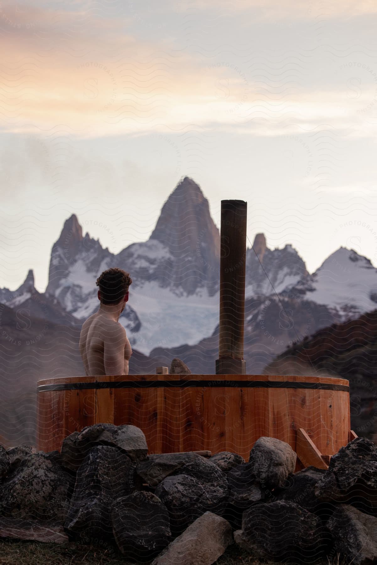 a man sitting in a hot tub with mountains in the background at sunset with a view of the mountains