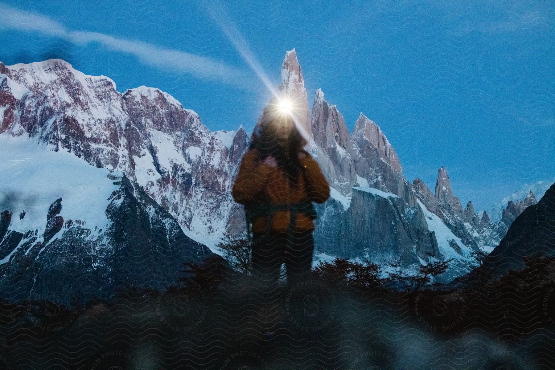 A woman is hiking through snow covered mountains as her headlamp glows