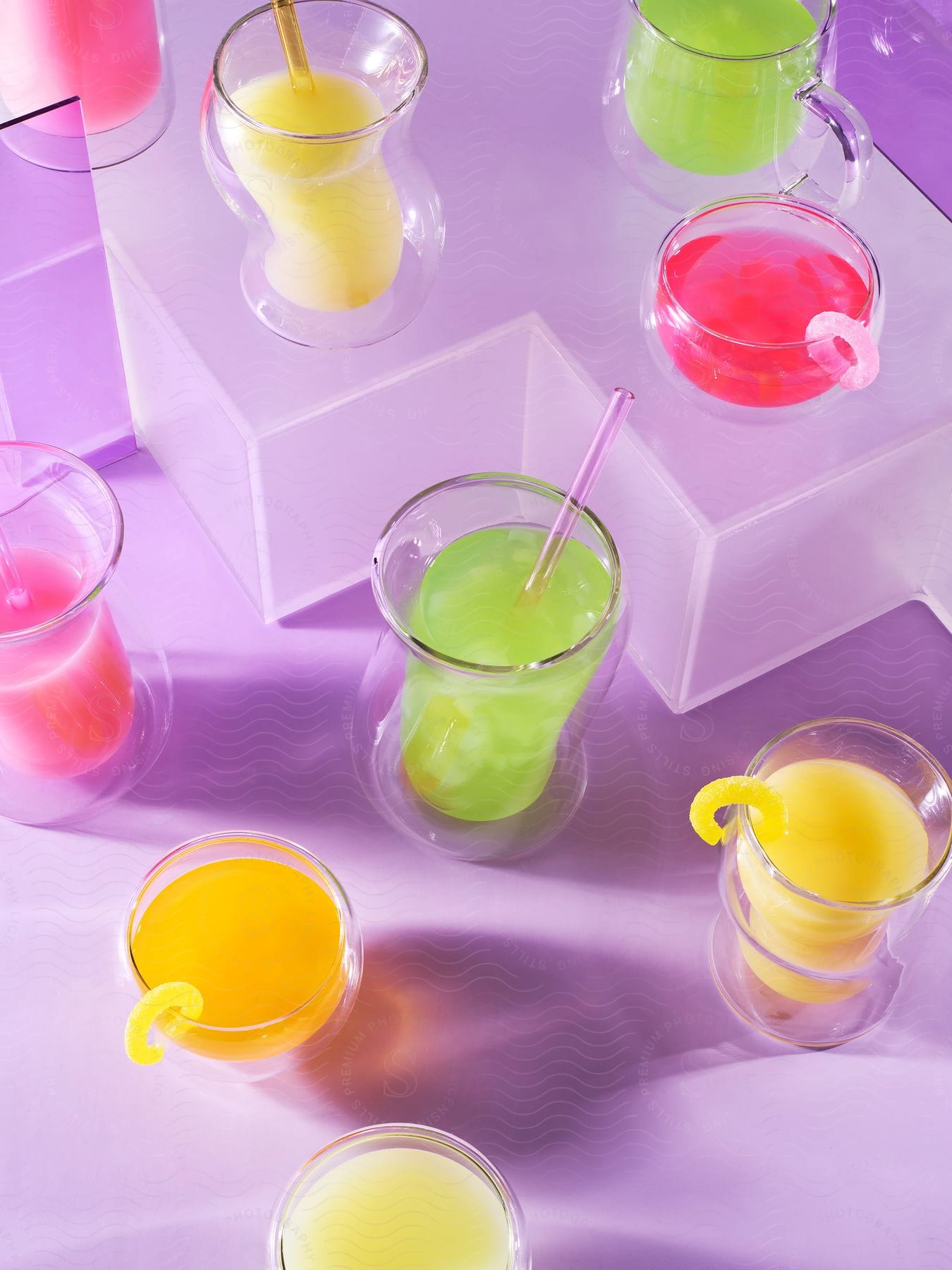 A group of clear cups contain bright pink, green and yellow beverages.