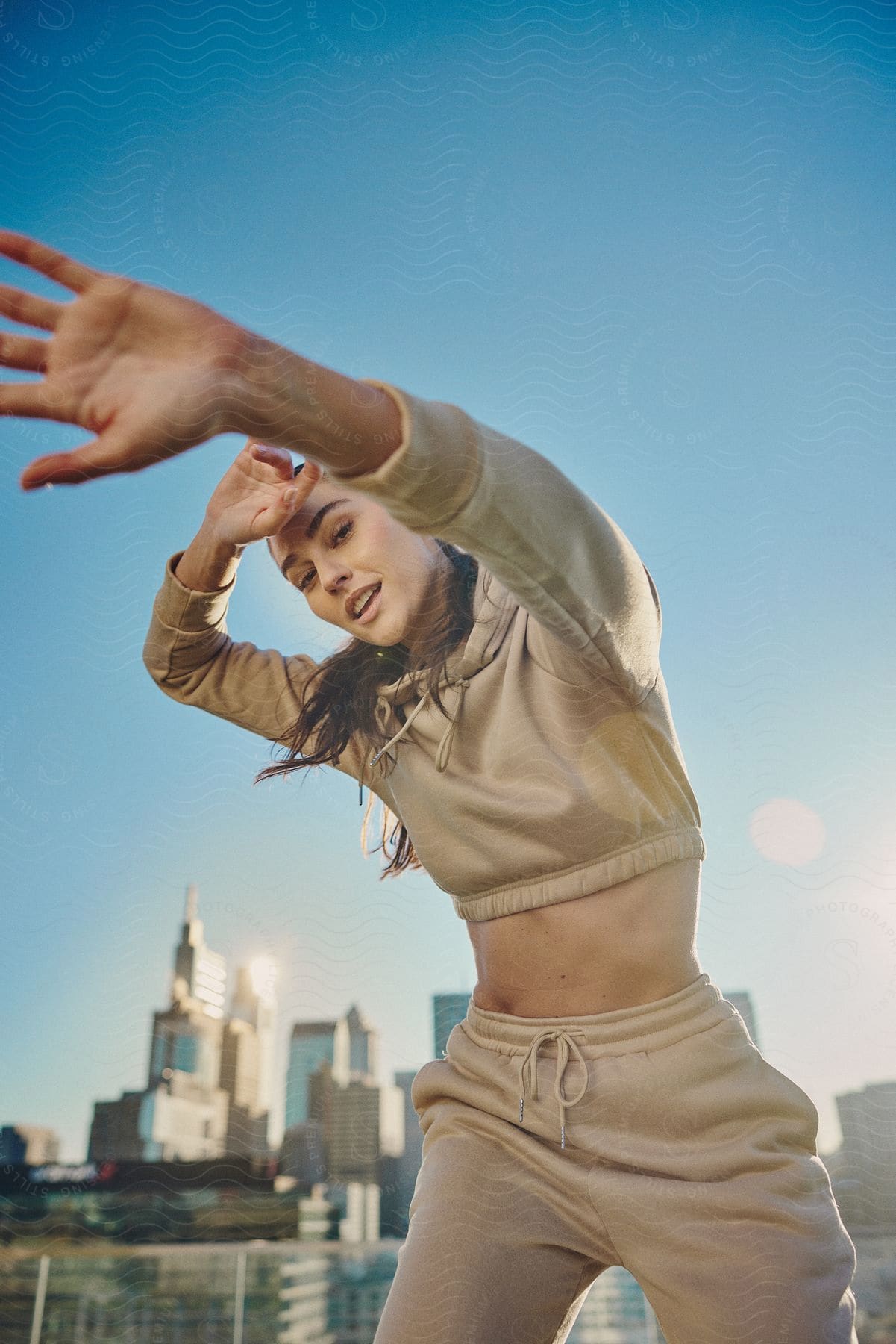 A womans arms are in the air as she dances with buildings and skyscrapers in the distance