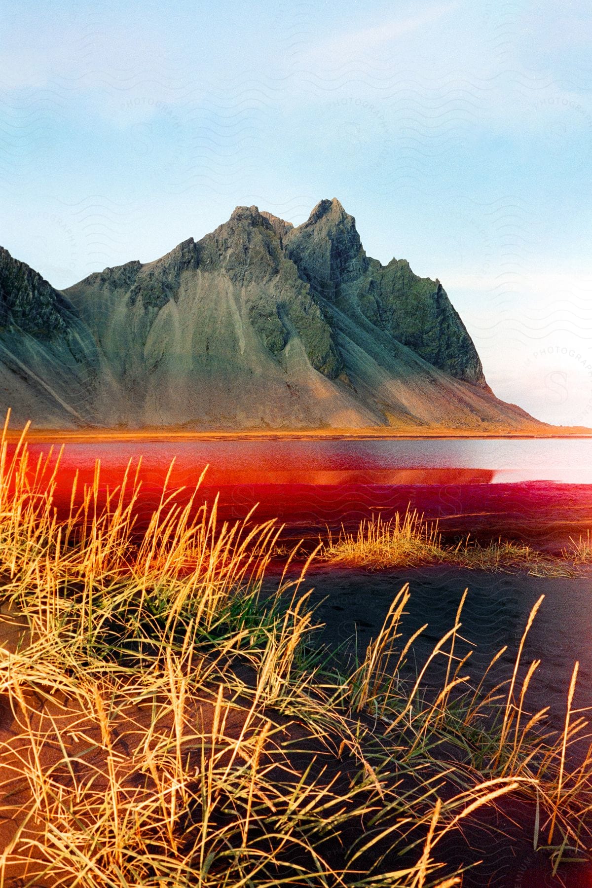 Landscape of a lake with neon red lighting, surrounded by peaks and mountains in daylight.