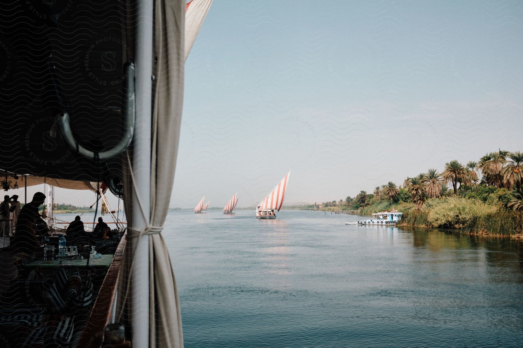 People sit in a building along the coast as sailboats sail near land