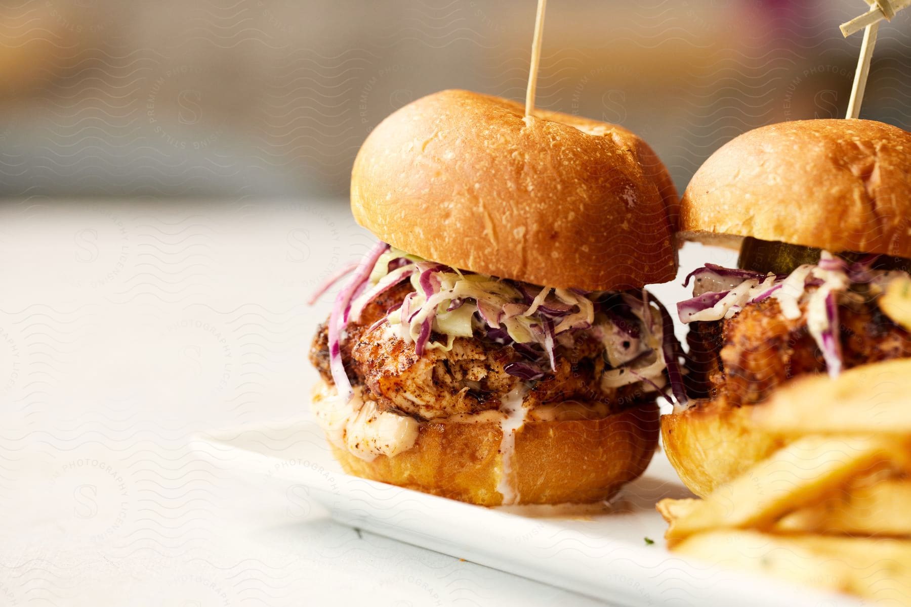 Two burgers sit on a plate with  wedge cut French fries.