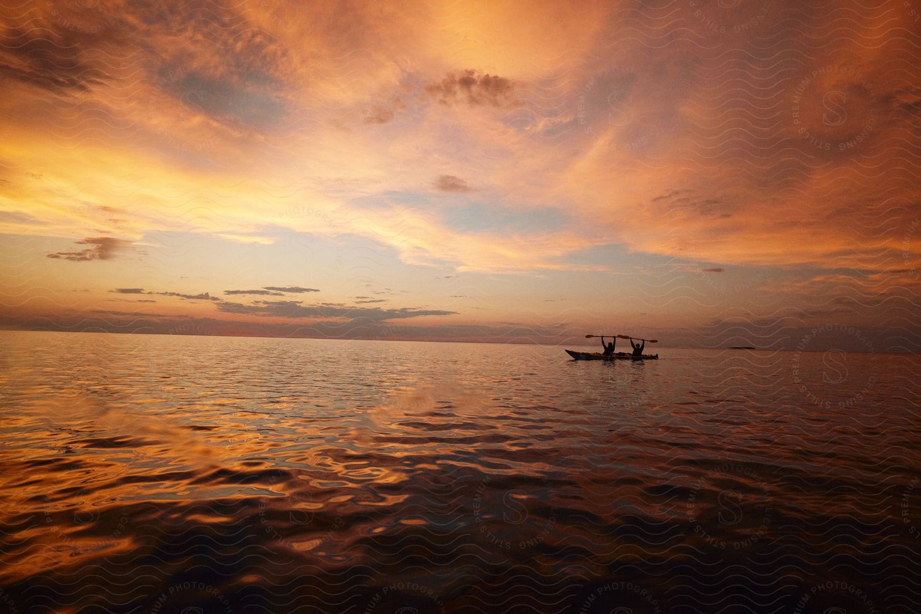 Silhouette of two men sitting in a canoe holding up their oars as the sun sets on the horizon