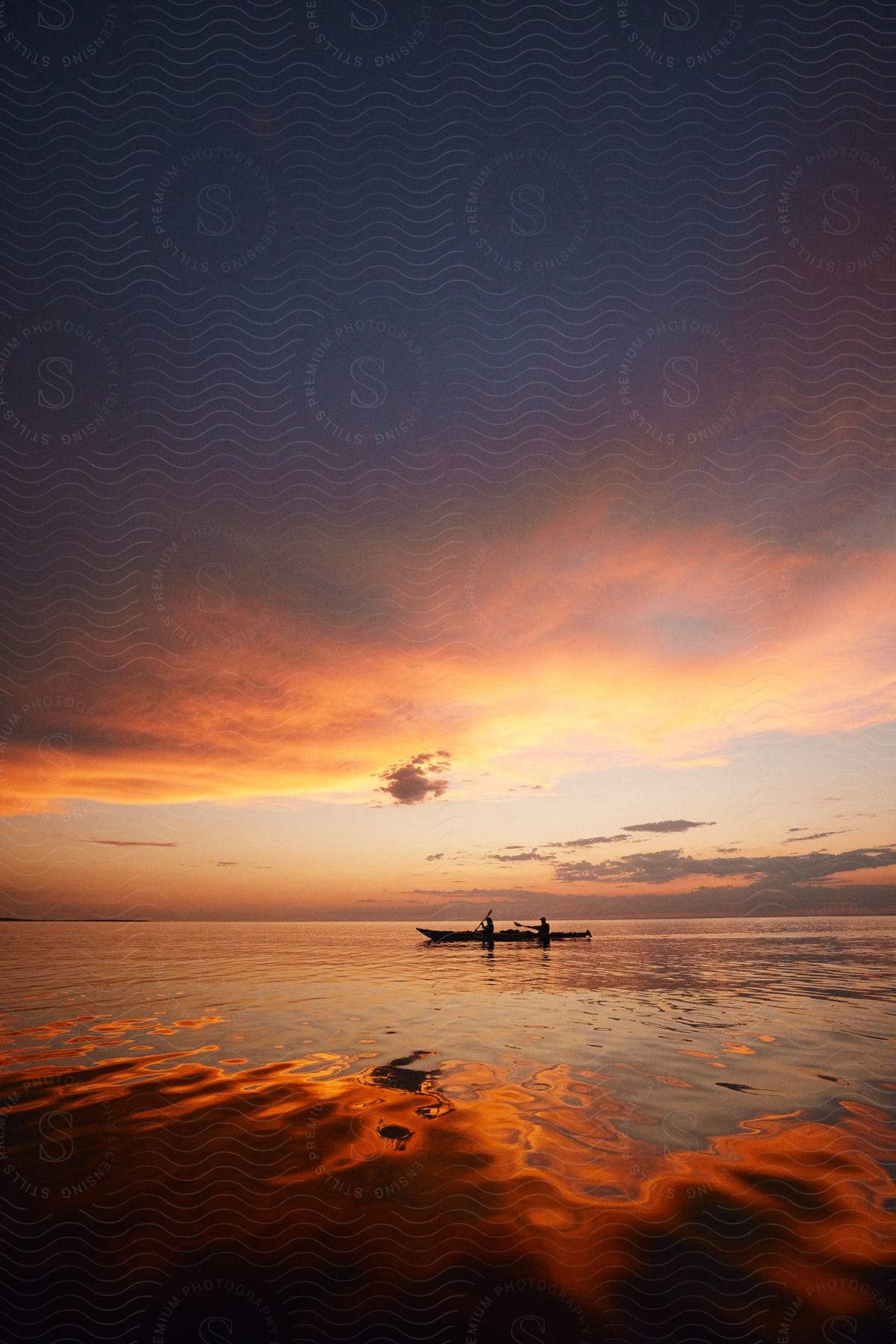 Two people sit silhouetted in boat on water reflecting bright afterglow.