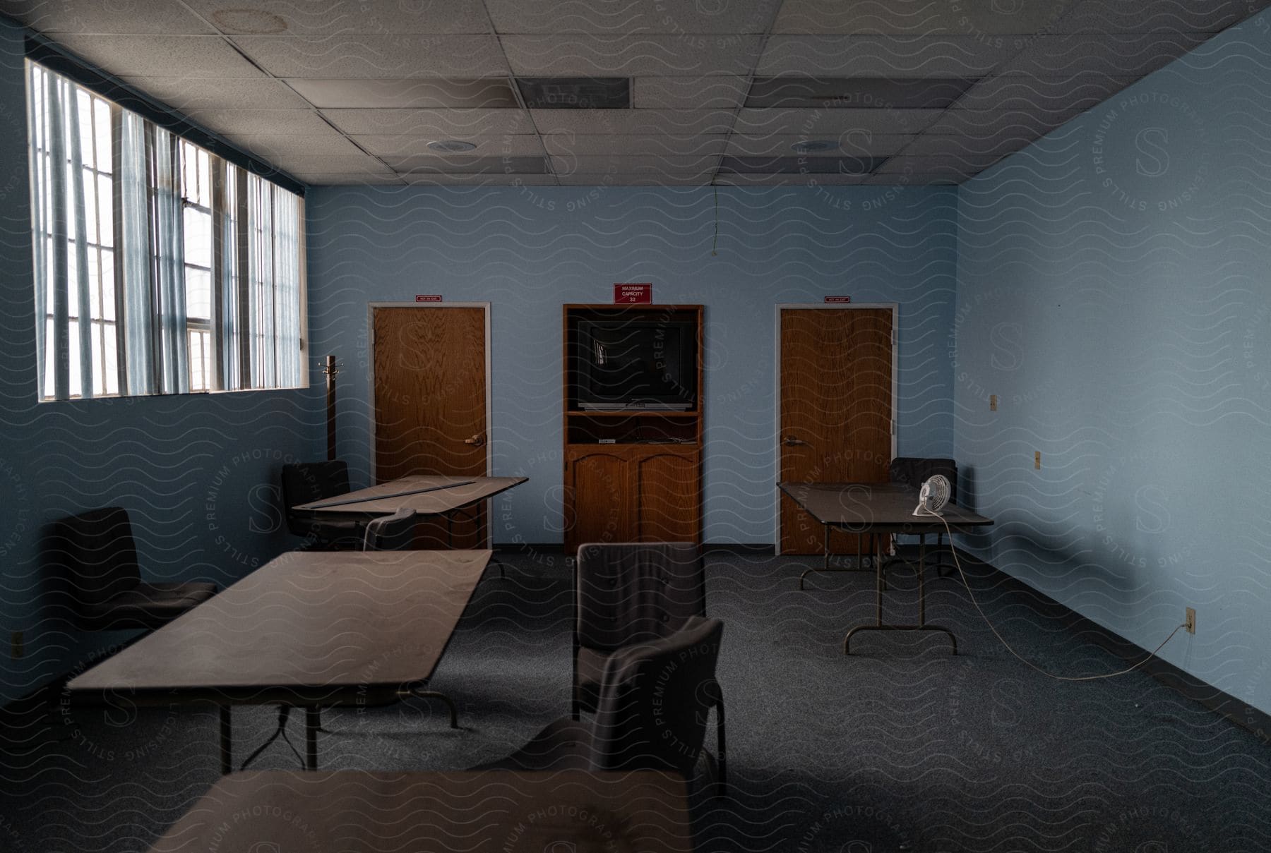 Small fan sits on one of multiple tables in long room containing a television.