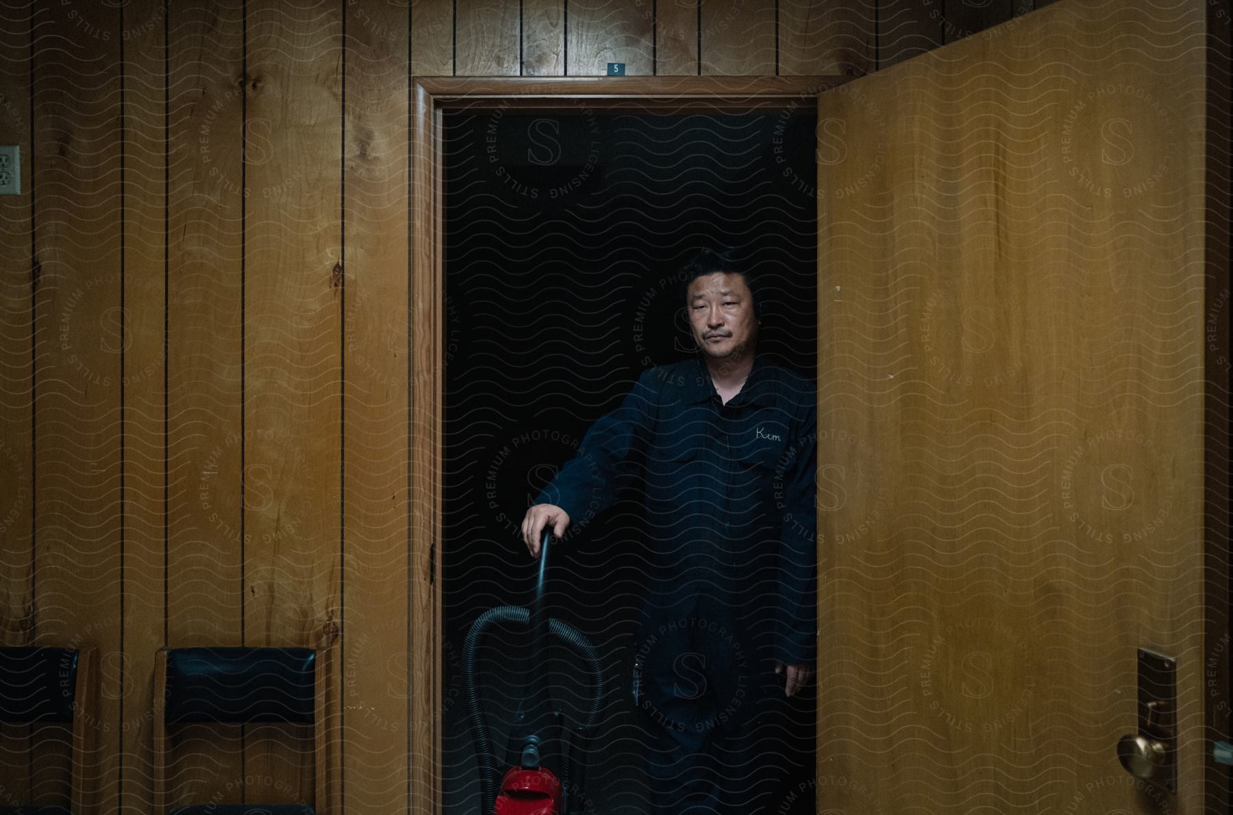 A maintenance worker standing in the office doorway with their right hand on a vacuum handle.