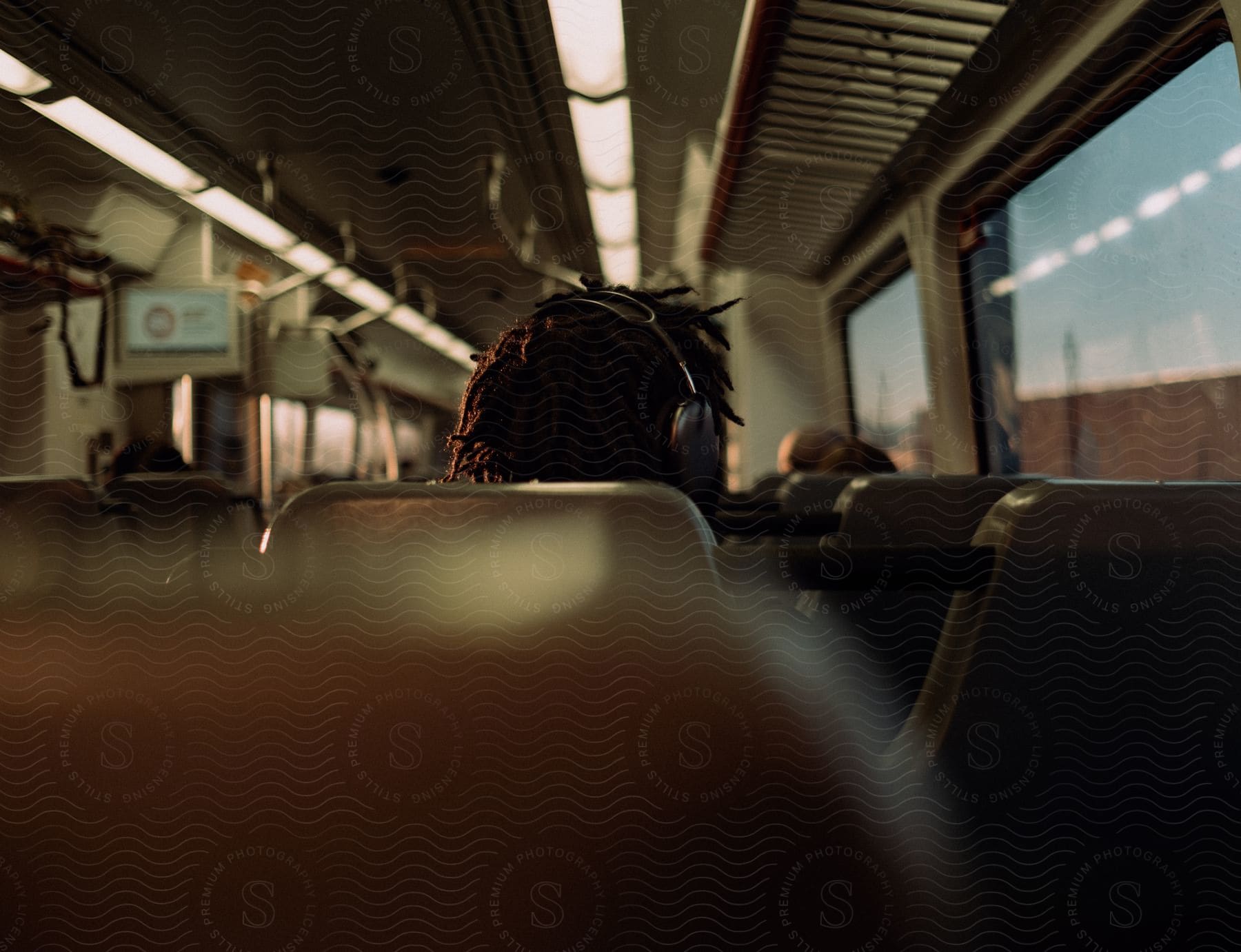 Stock photo of a person wears headphones while riding on a passenger train during the daytime.