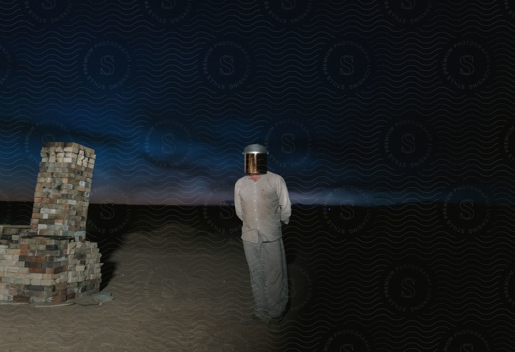 A man wearing a helmet and normal clothing stands in the sand next to a brick fire place