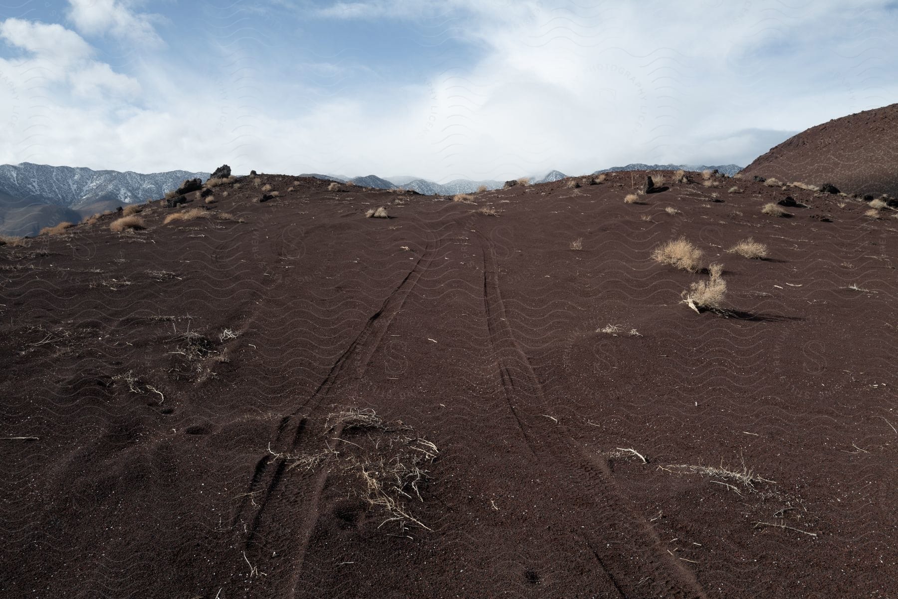 Dirt and tire tracks cover a barren hill on a partly cloudy day.