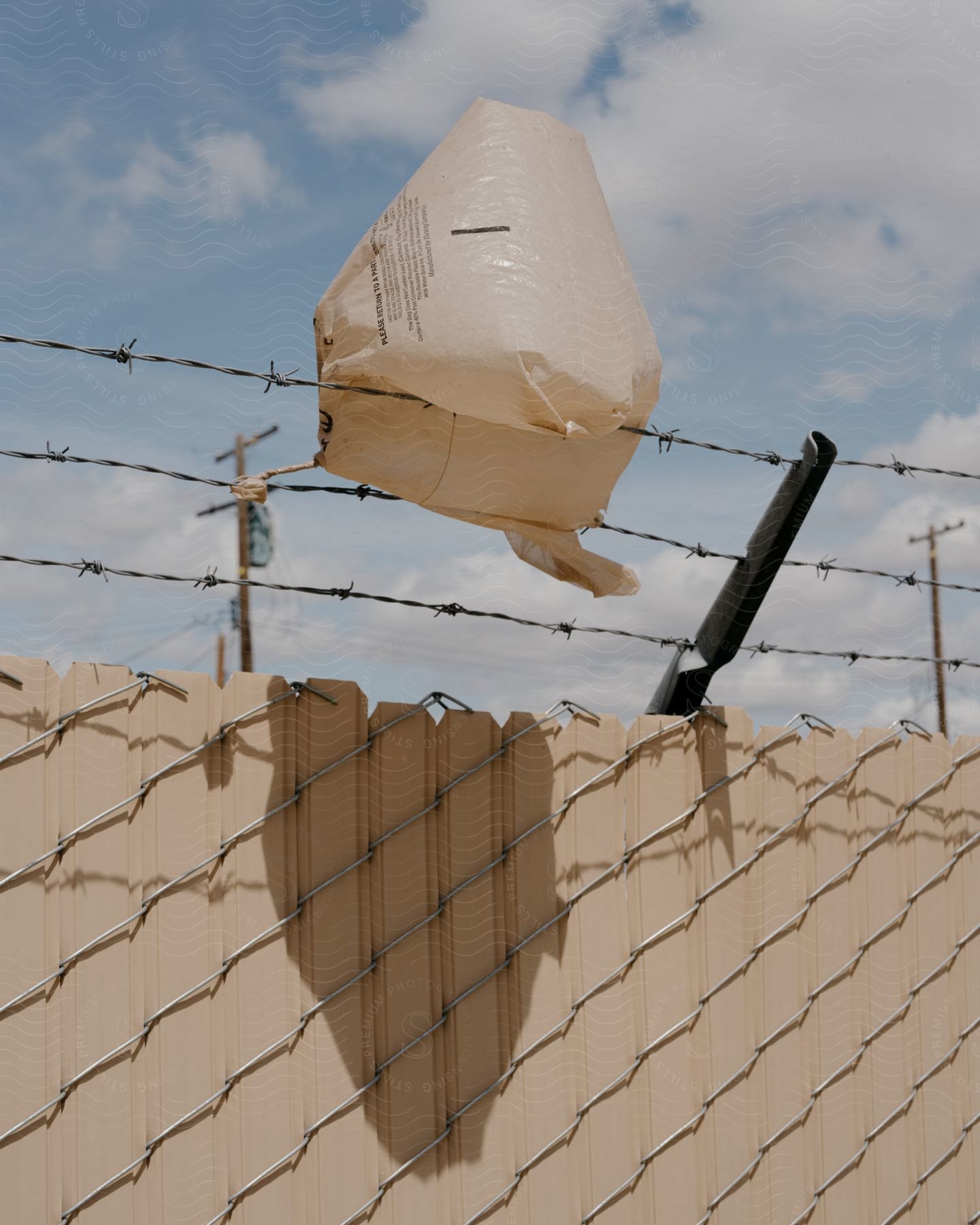 Inflated plastic bag rests on barbed wire at top of fence on a cloudy day.