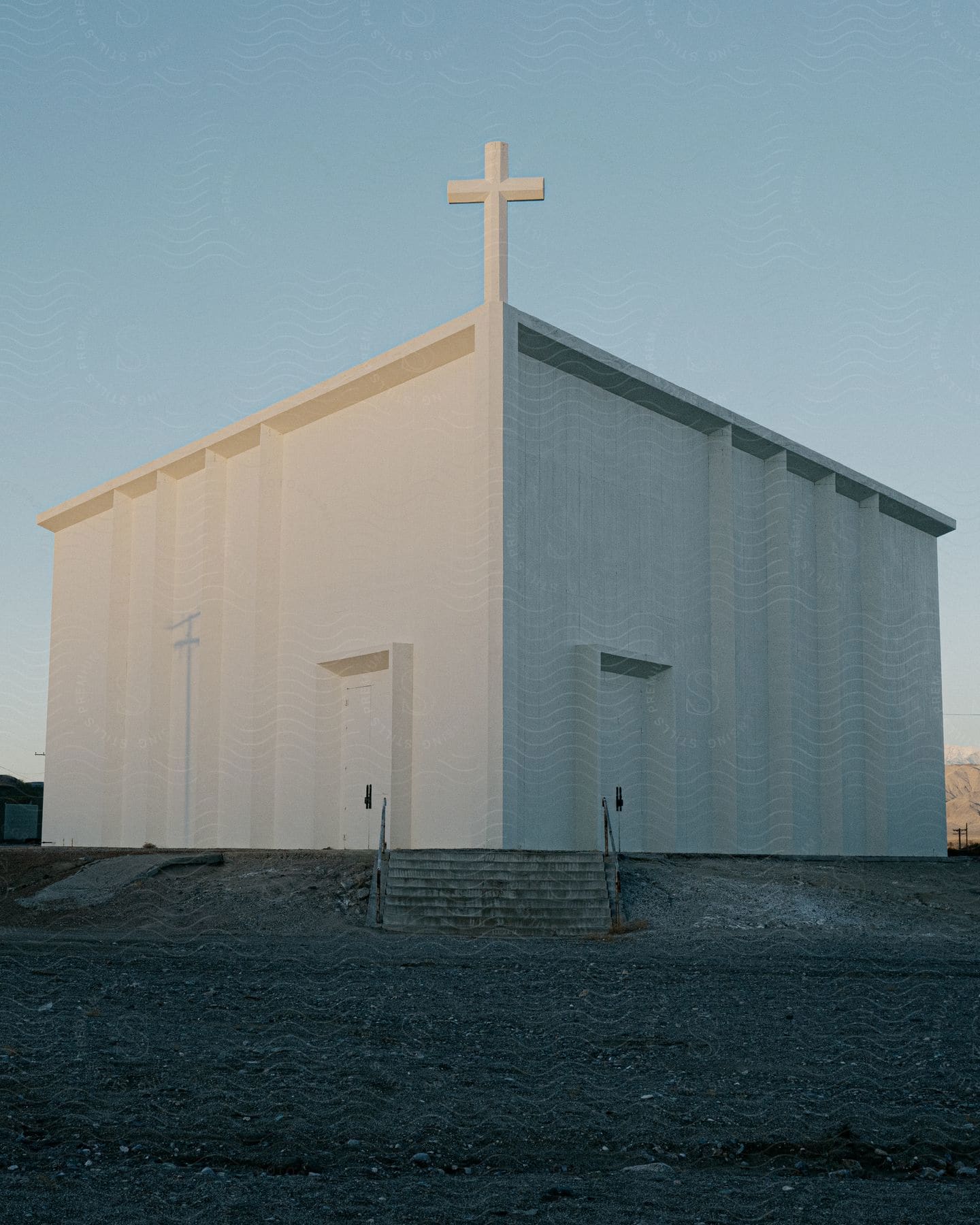 A white church building contains a white cross on the roof on a clear, sunny day.