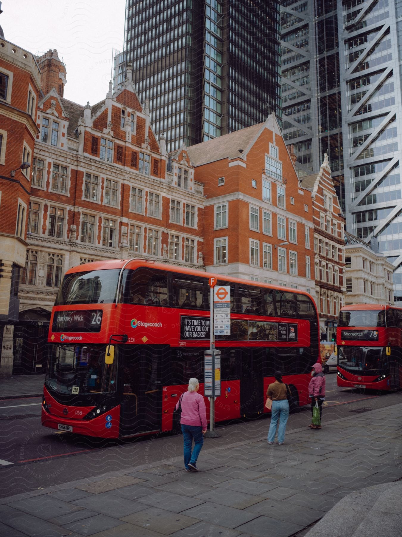 People are standing on the street as buses pass by