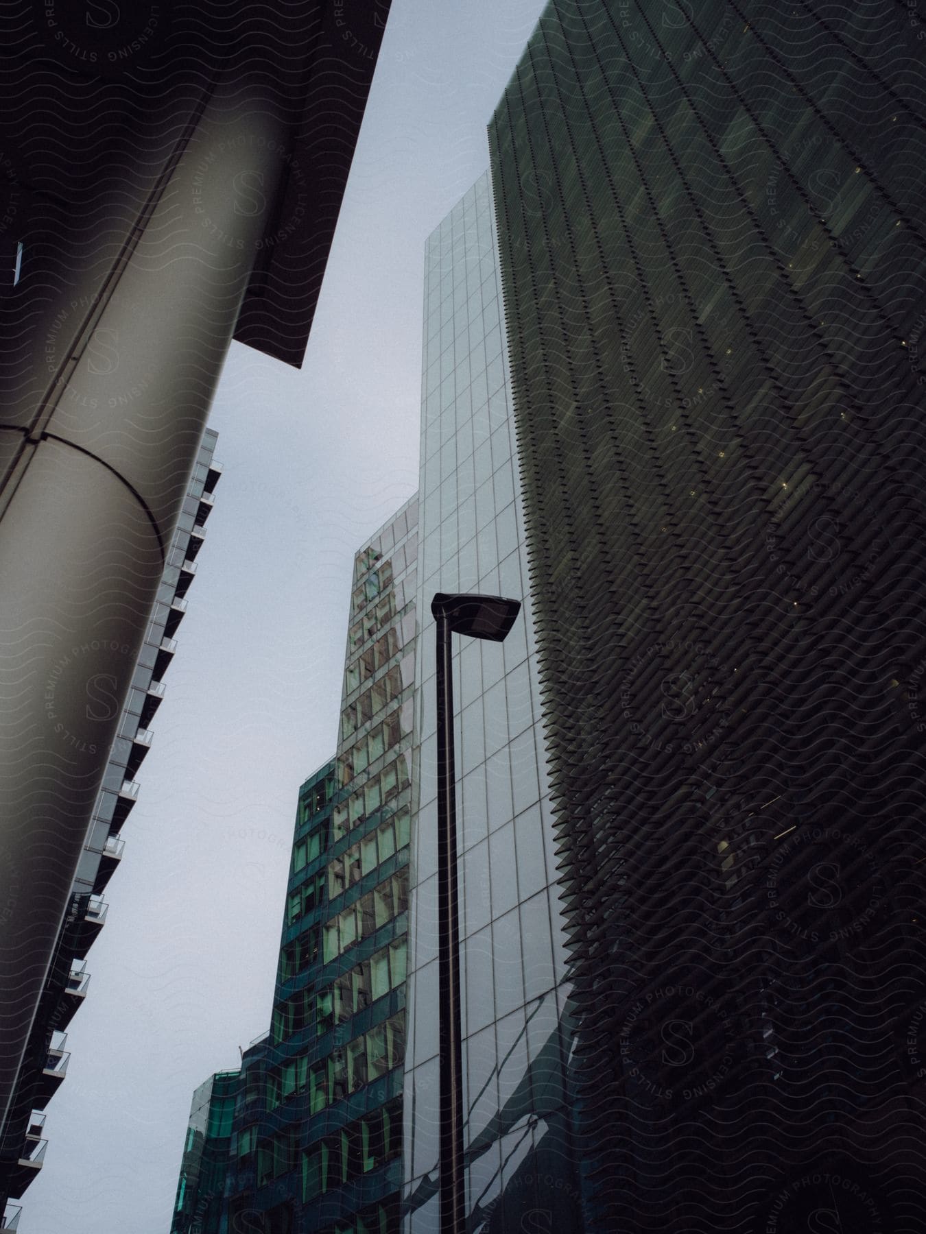 Skyscraper mirrors gleam against cloudy skies, a lone streetlamp pierces the grey.