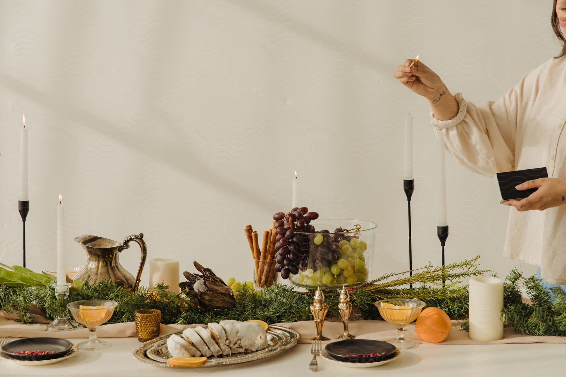 A woman stands over a dinner table holding a match as she lights candles