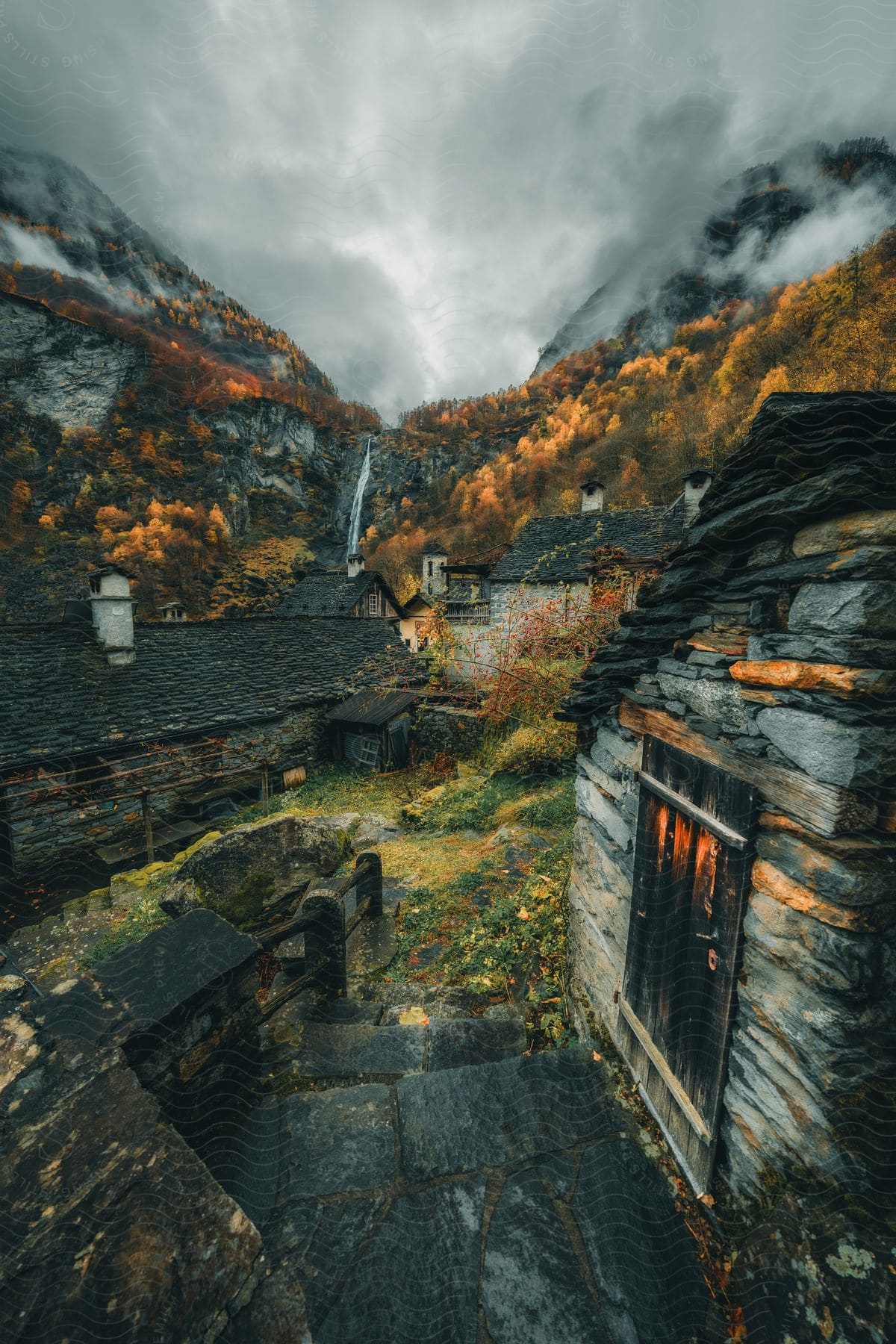 A small rural town with houses made of stacked stones and trees that have red leaves