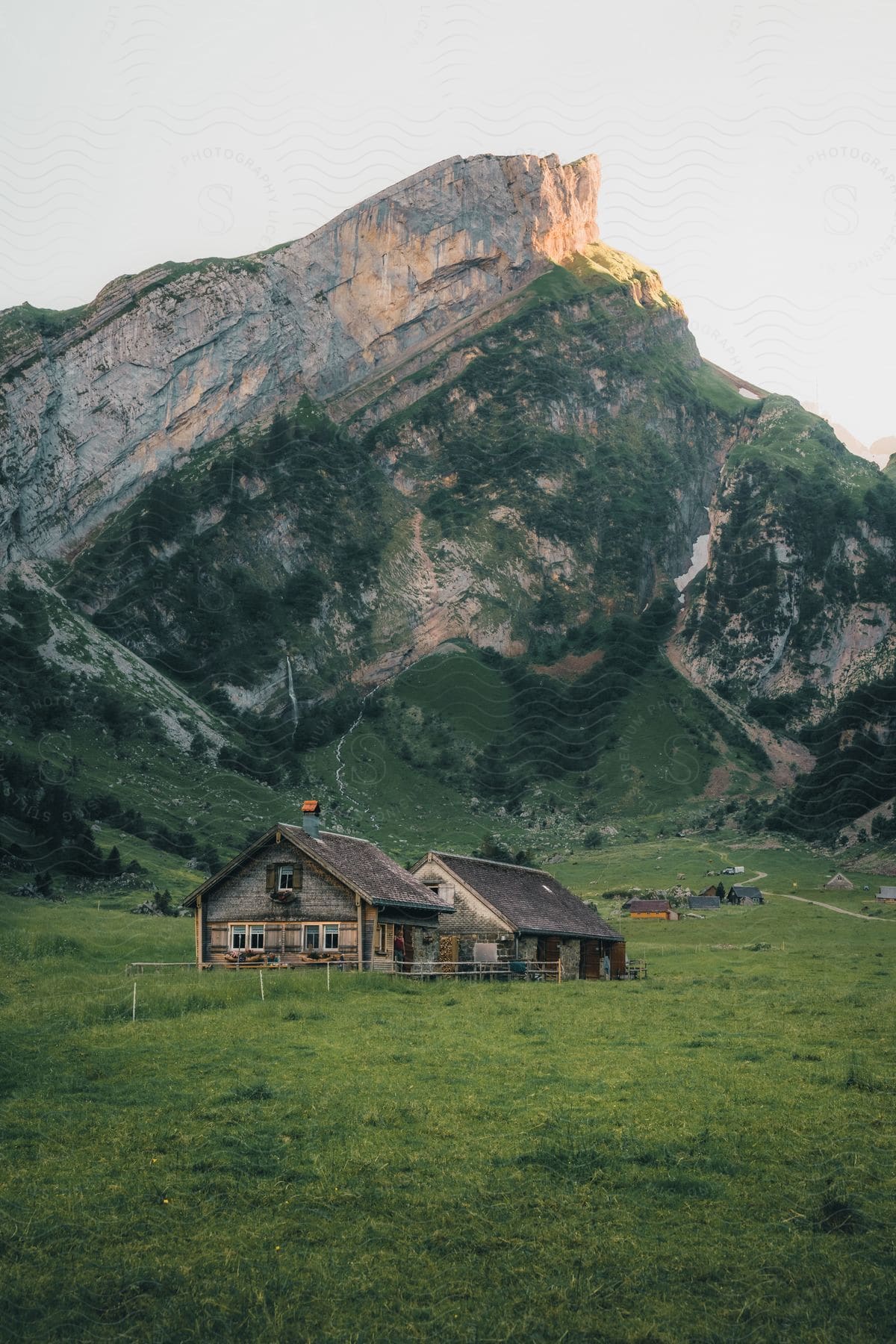 Stock photo of a wooden cabin stands in a field with a mountain in the background.