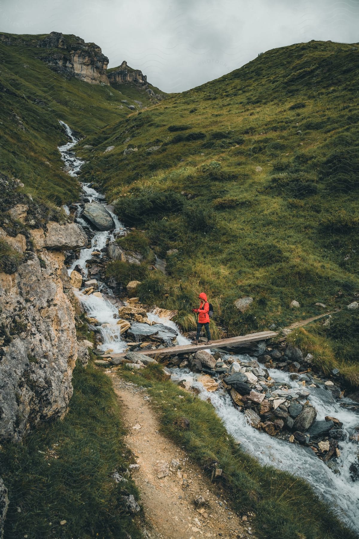 a woman wearing a jacket is crossing a stream on the mountain