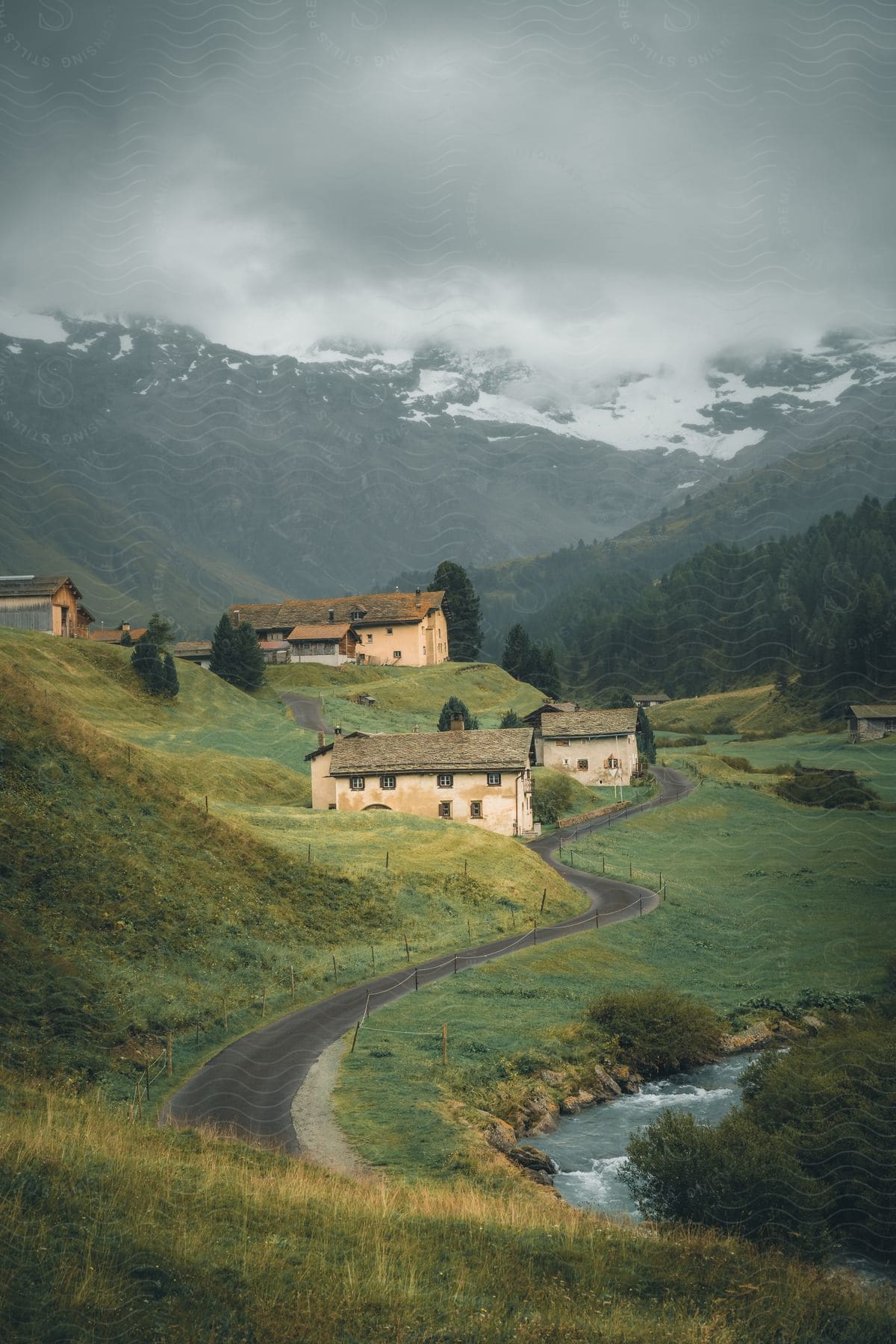 A twisting road cuts through emerald fields, past a sleepy town of weathered homes, leading to a cloud-kissed mountain in the distance.