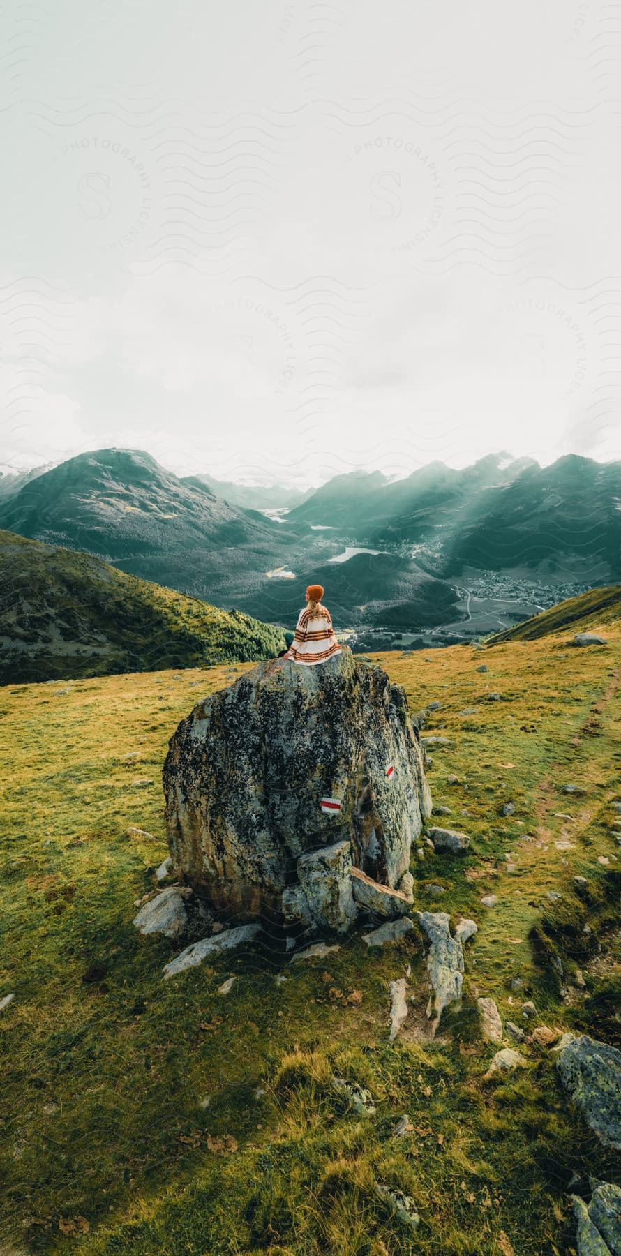 A woman sits on tops of a large rock formation overlooking mountains