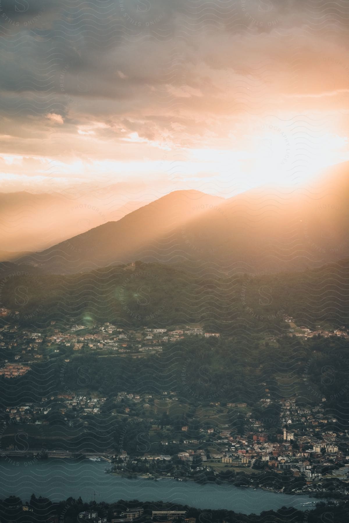 aerial of the sun shining above a high mountain range overlooking a coastal town.
