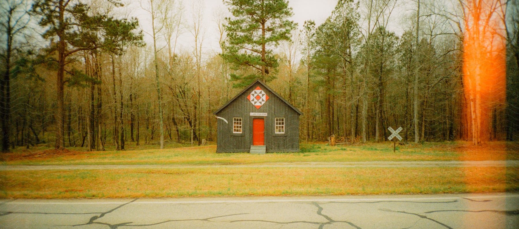 A house with a symbol above the door stands in a field surrounded by woods