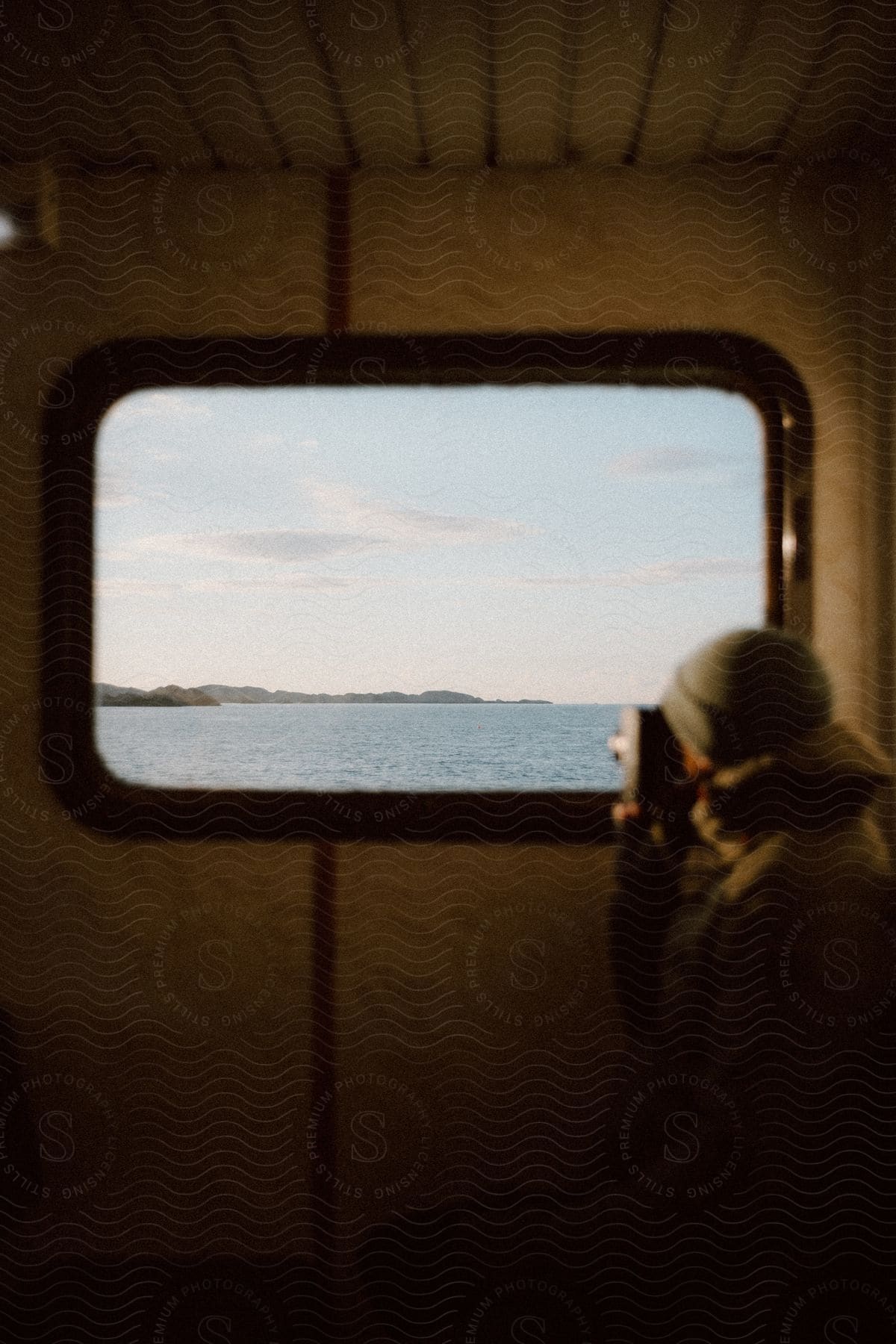 Winter-clad photographer captures a timeless vista of water through a boat window, using a vintage film camera.
