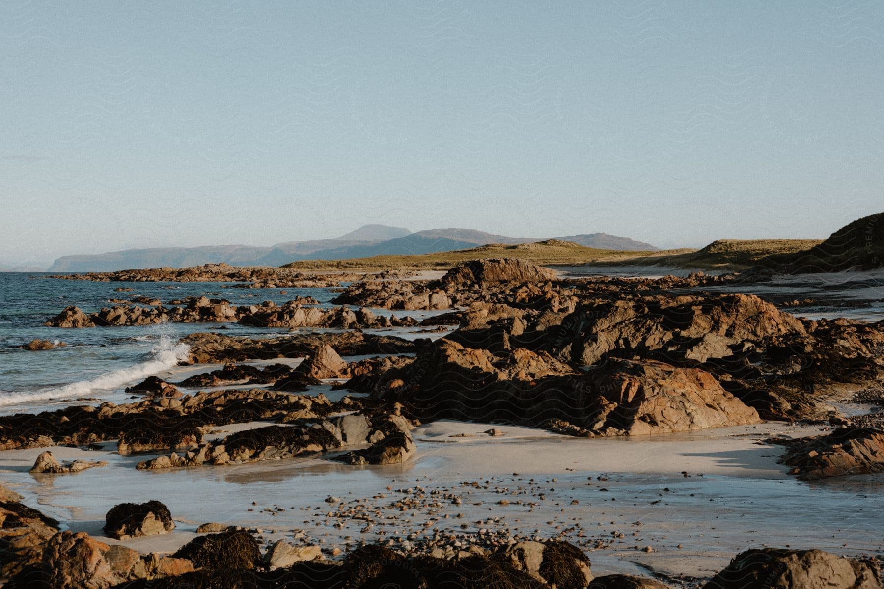 Ocean waves crash against a rocky beach on a clear day.