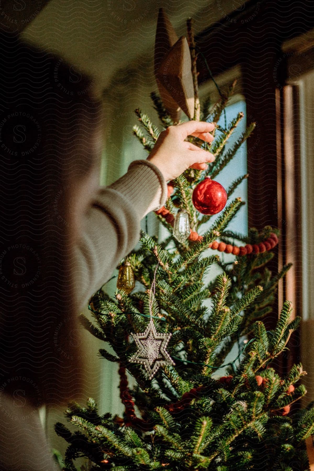 A woman hanging a christmas ornament on a tree.