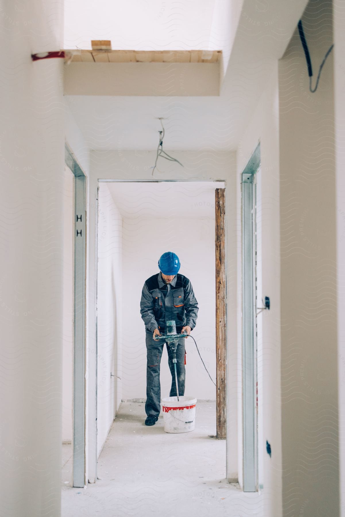 A construction worker is standing in a room holding a machine over a bucket