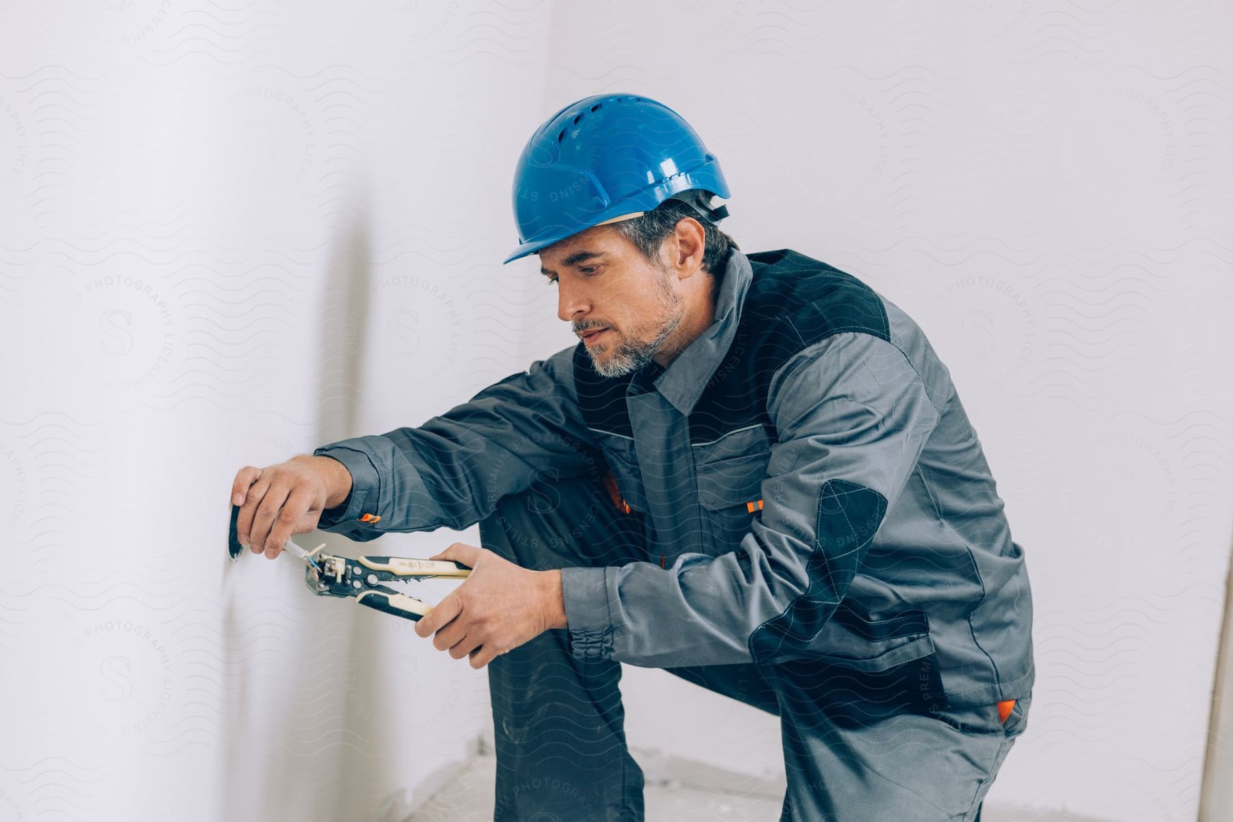 An electrician holds wires from inside a wall with pliers
