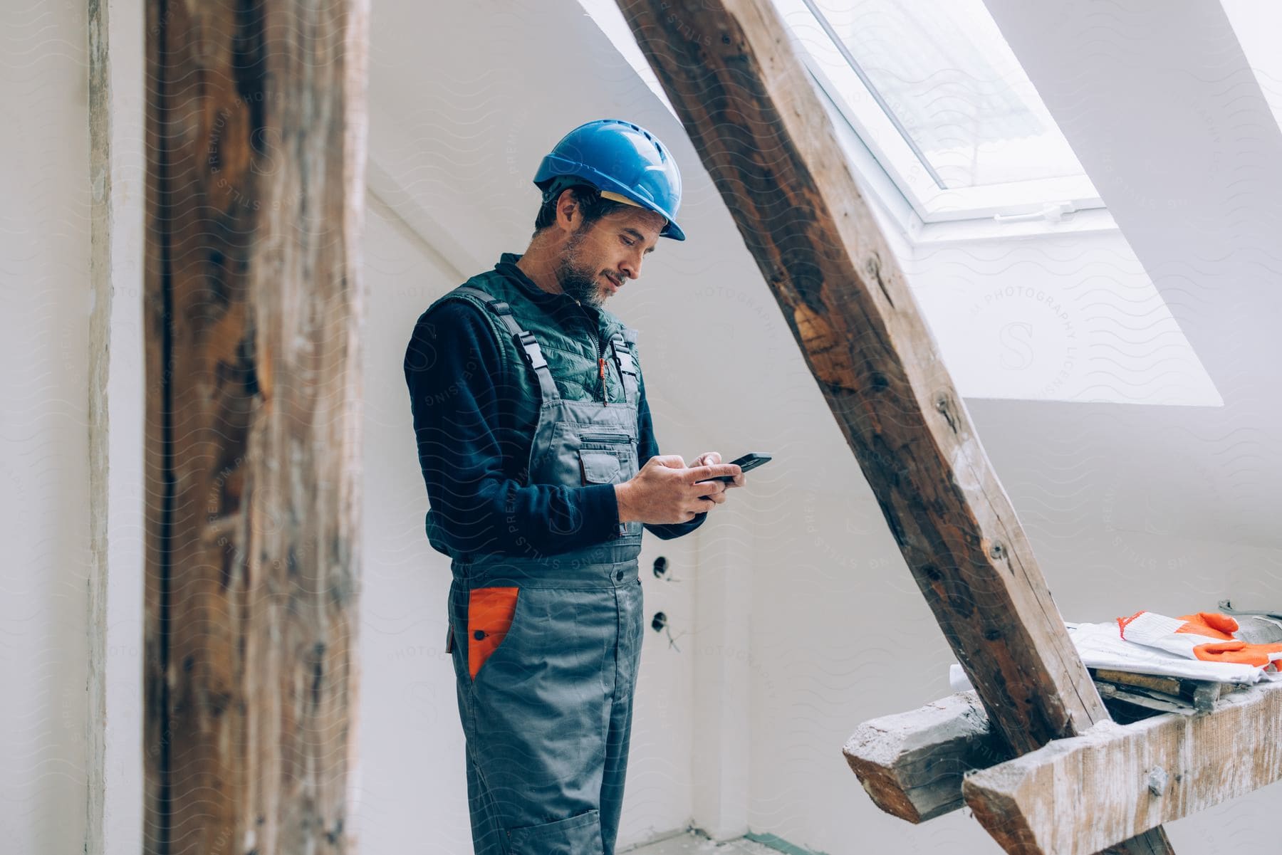 Construction worker uses smartphone while standing near reinforcing wooden structure in building.