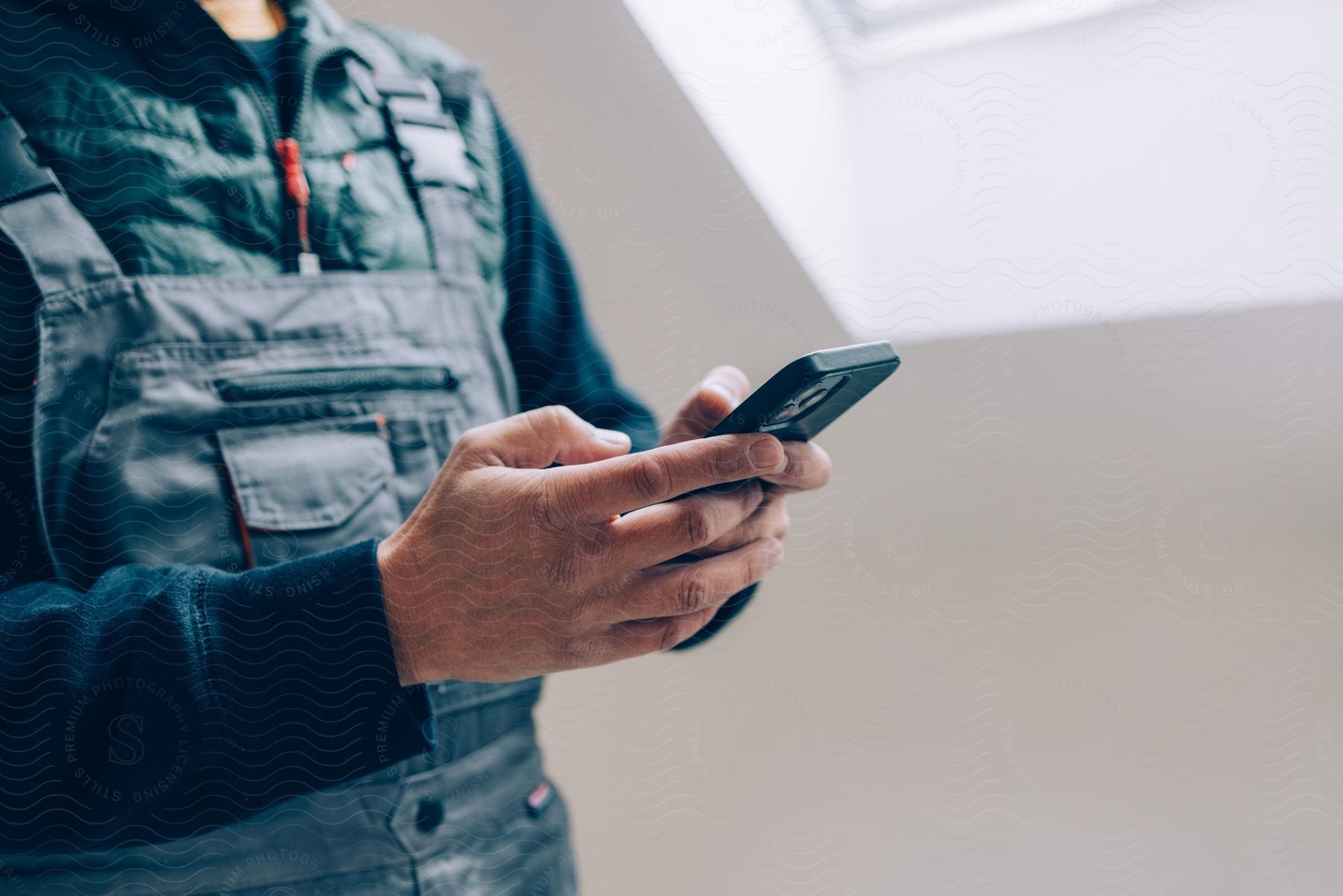 A man wearing overalls over down clothing holding a phone near a skylight