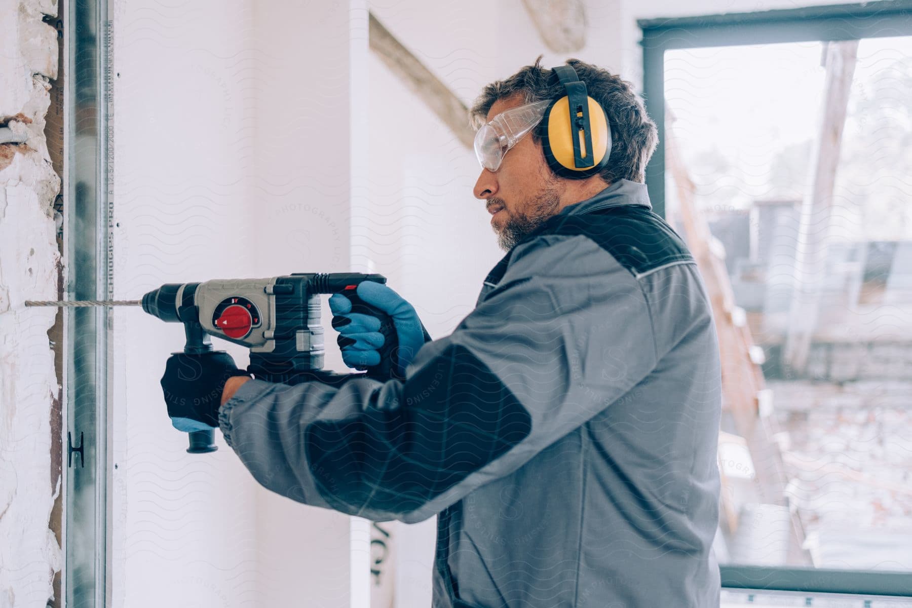 A carpenter wearing safety gear drills a hole into a wall during a home renovation project.