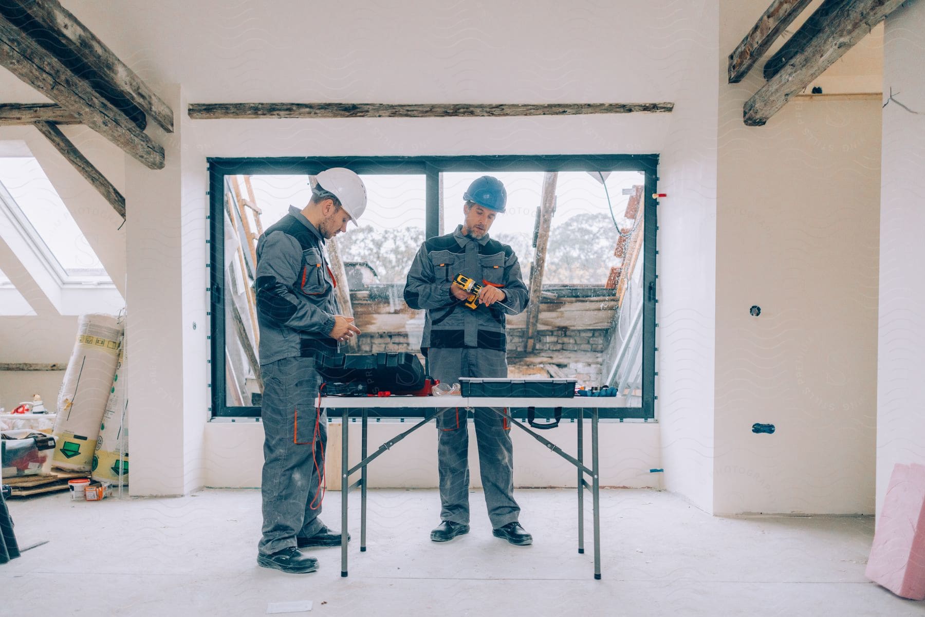 Two men with tools inside a house amidst construction.