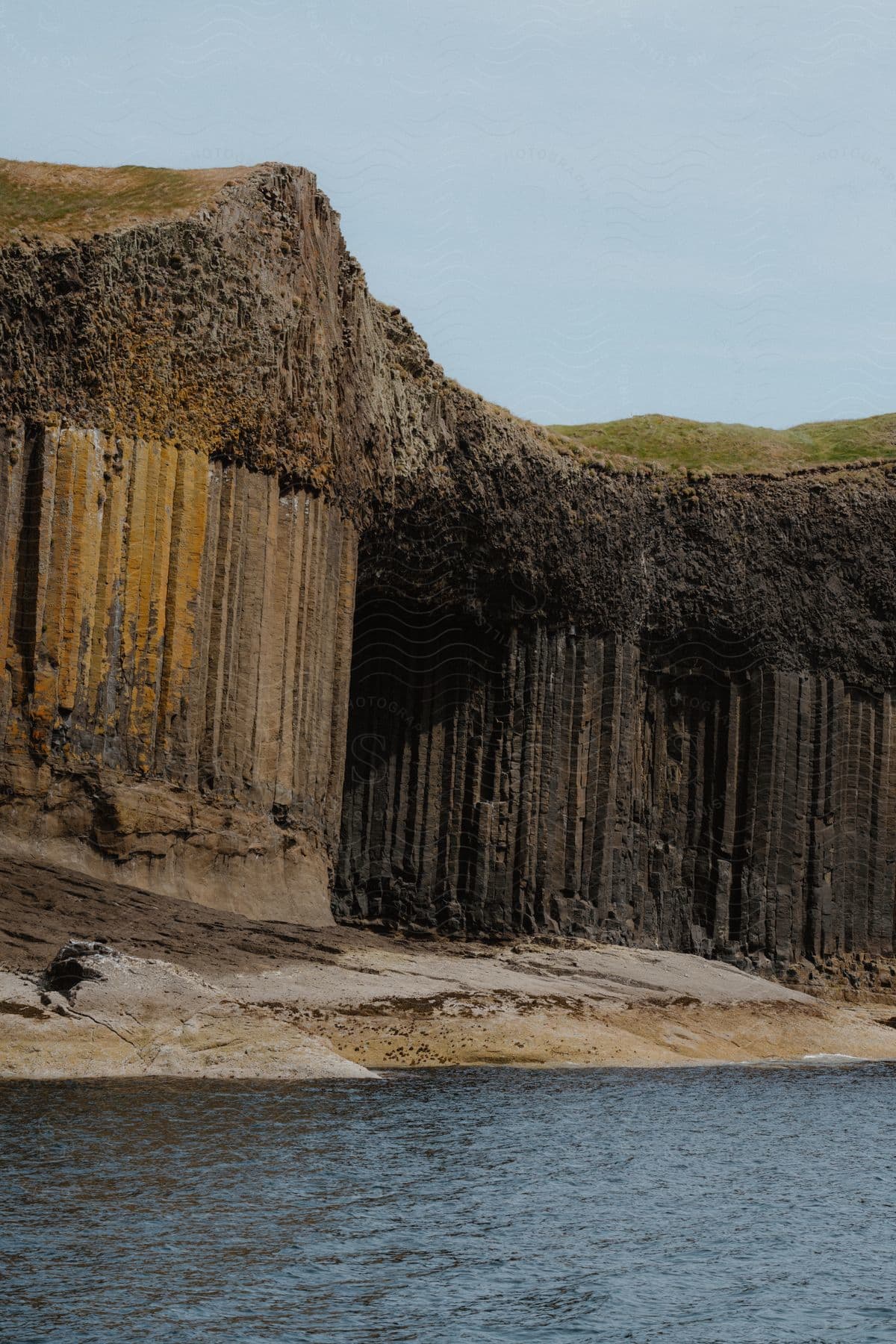 Columnar basalt formations on a cliff beside calm water.
