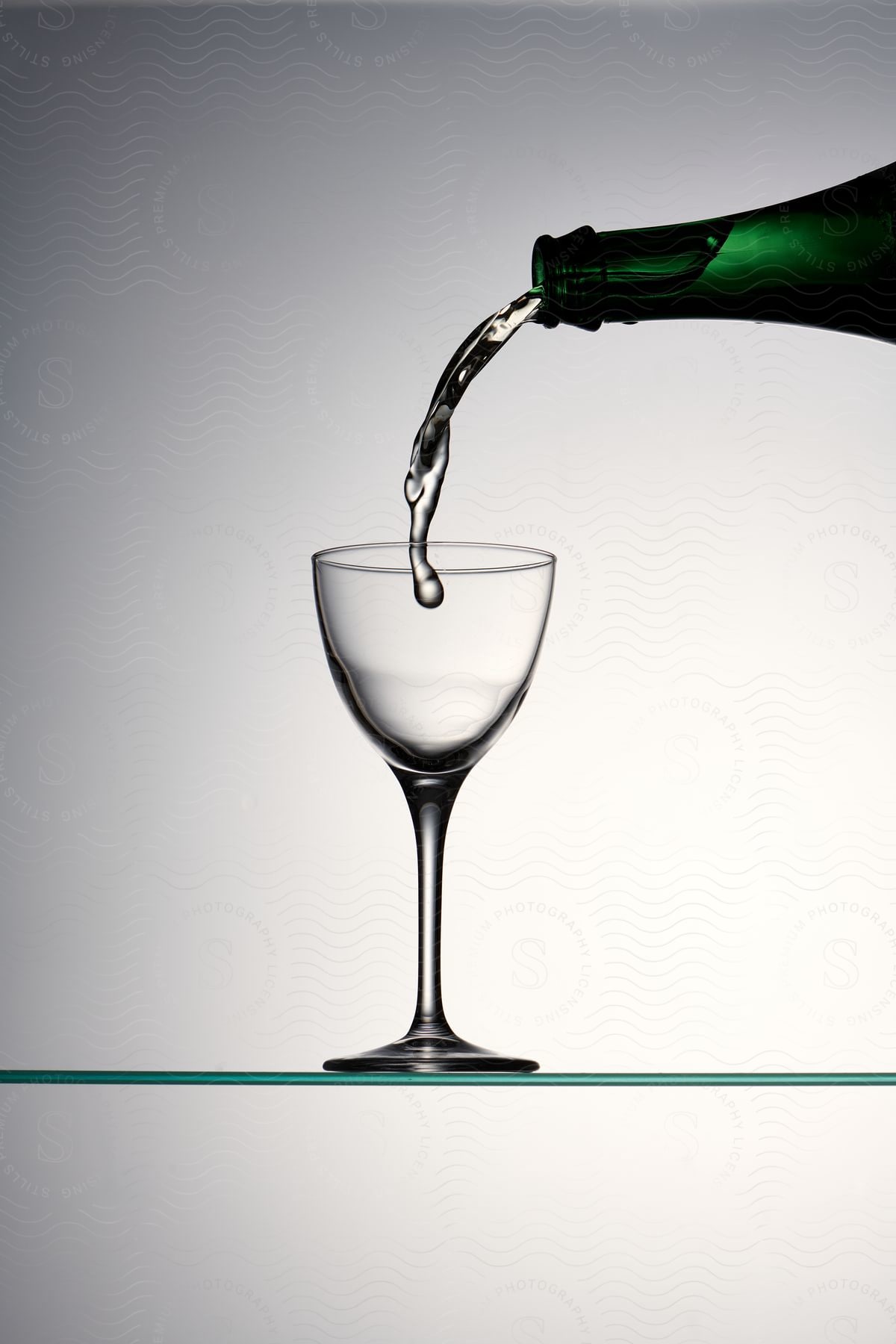 Pouring liquid from a green bottle into a crystal wine glass.