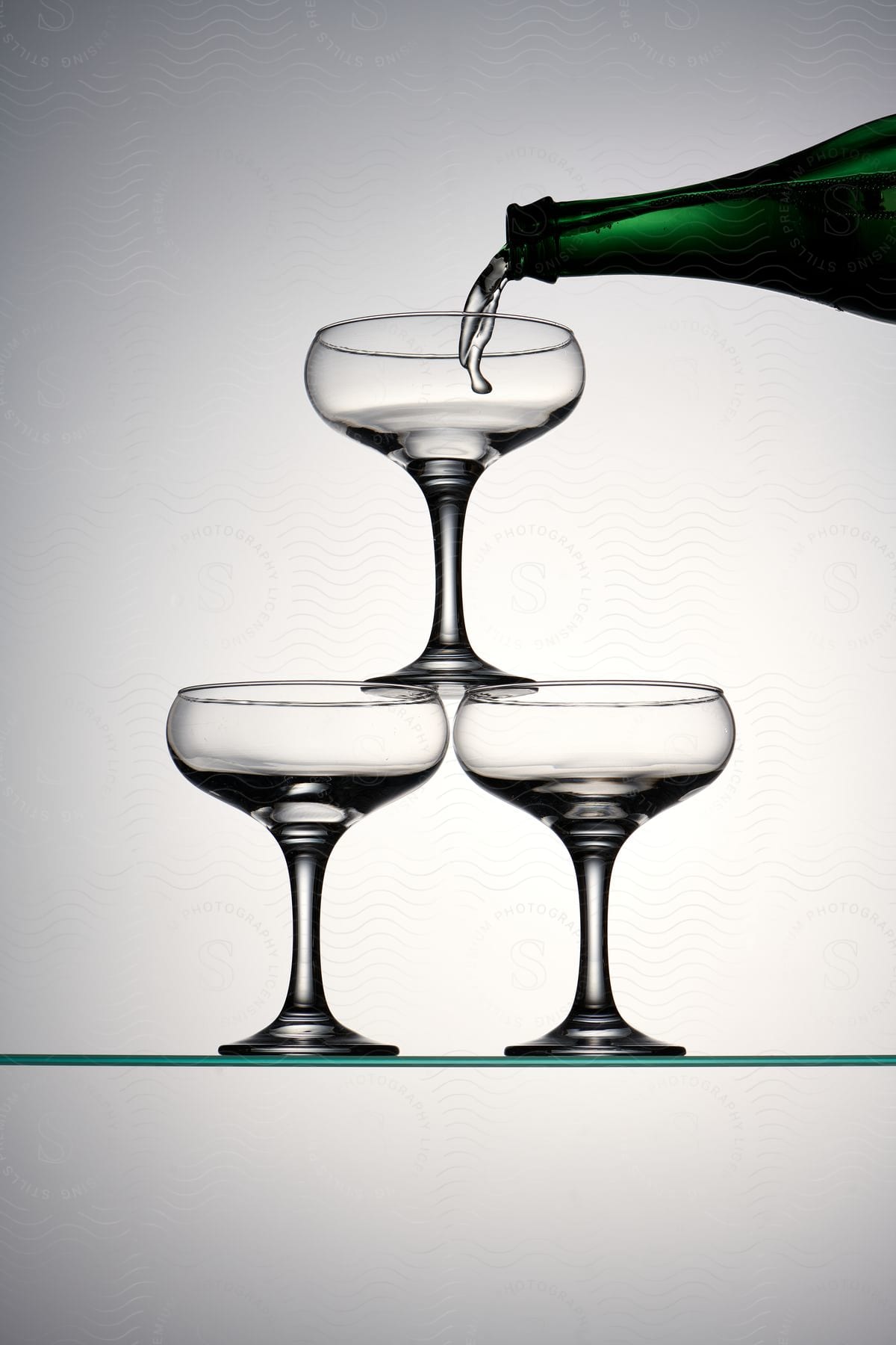 a green bottle of wine is being poured into three wine glasses on a table with a glass bottom