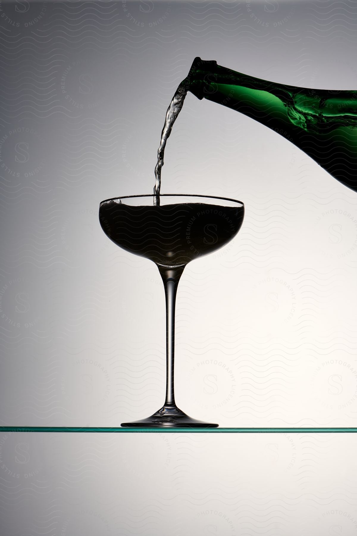 Close up of a stream of beverage flowing from green bottle into a goblet.