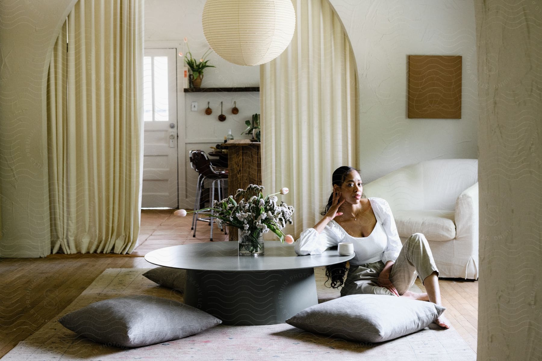 A woman sits on the floor of a living room leaning her elbow on a coffee table.