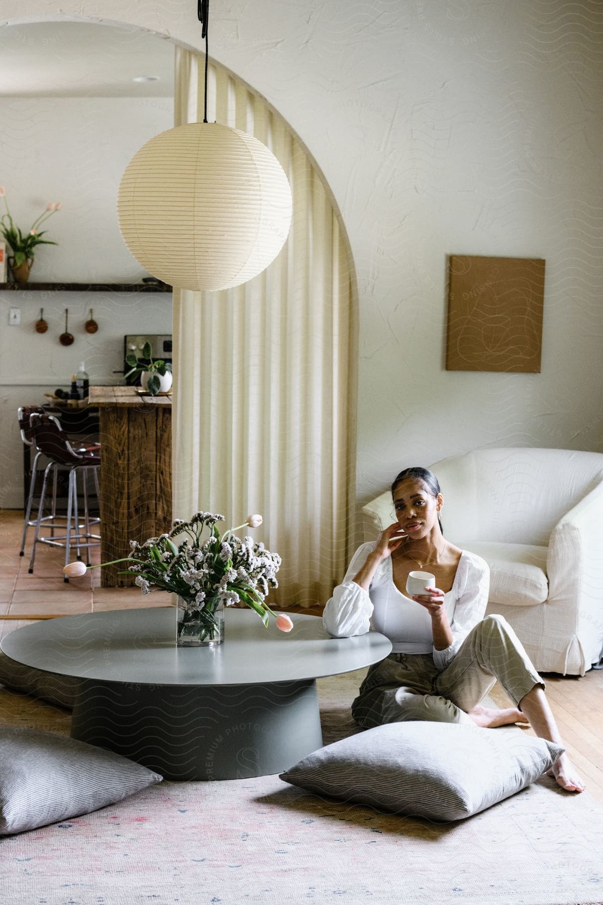 Woman relaxes on living room floor, coffee mug in hand, couch behind and kitchen in view.